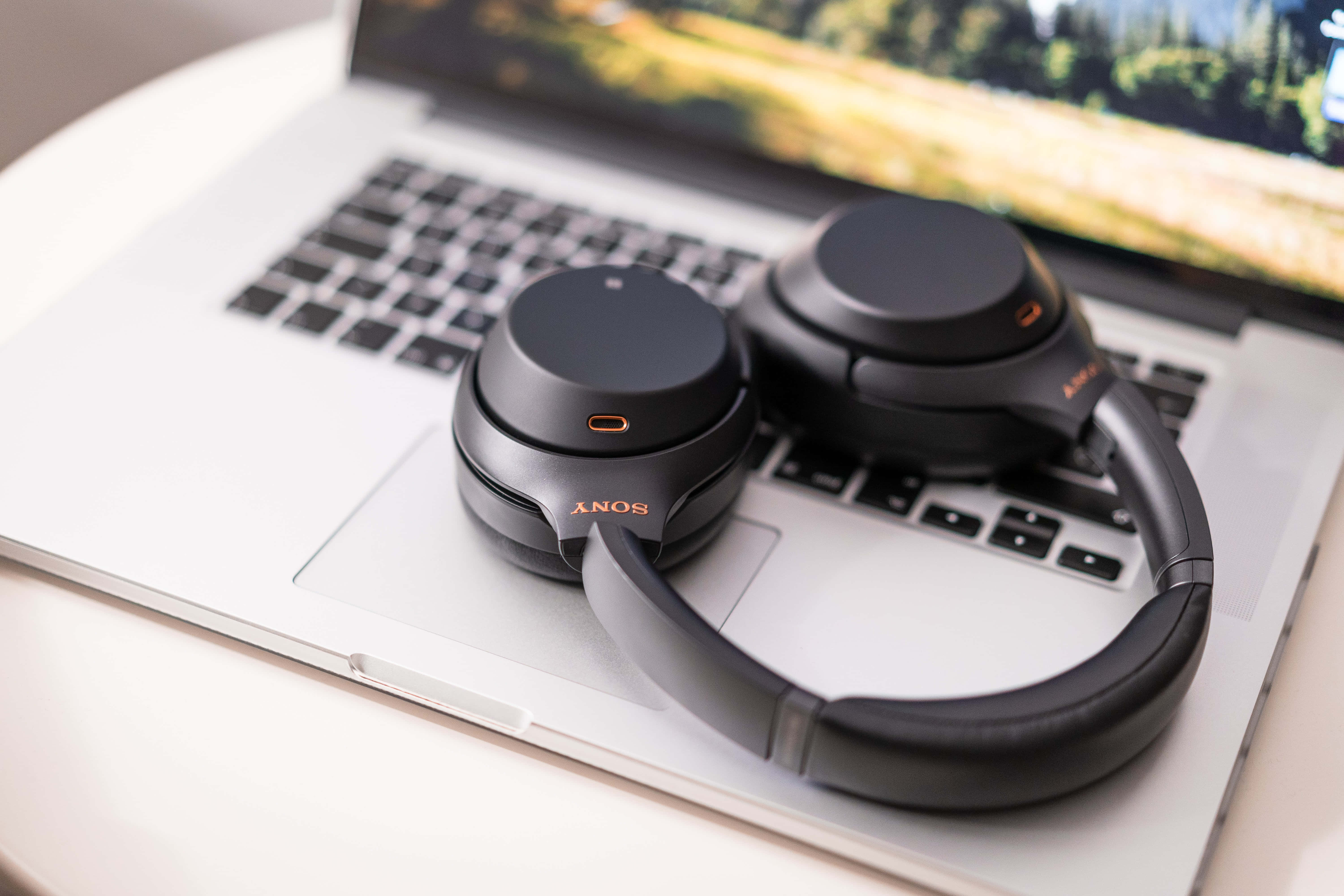 桌布 壁紙 — 黑色Sony頭戴式耳機放在一部顯示陽光照射田野場景的銀色筆記型電腦上。