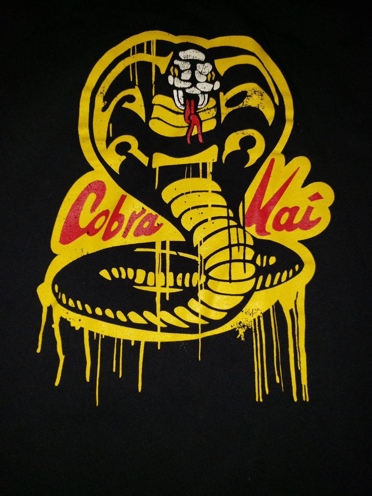 Cobra Kai Phone 桌布 壁紙 — 黑色T恤上帶有滴蛇設計的大膽黃色和紅色Cobra Kai標誌。