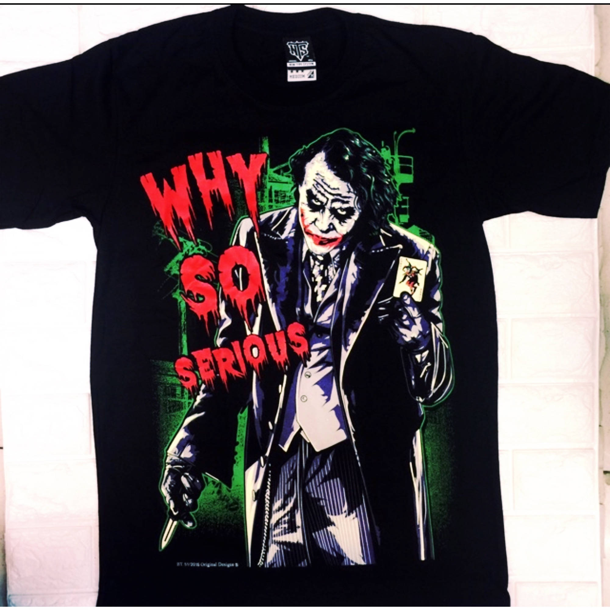 Why So Serious Joker 桌布 壁紙 — 黑色T恤展示一個風格化的小丑，手持刀和小丑牌，滴落的紅色文字寫著「WHY SO SERIOUS」，背景是綠色城市景觀。