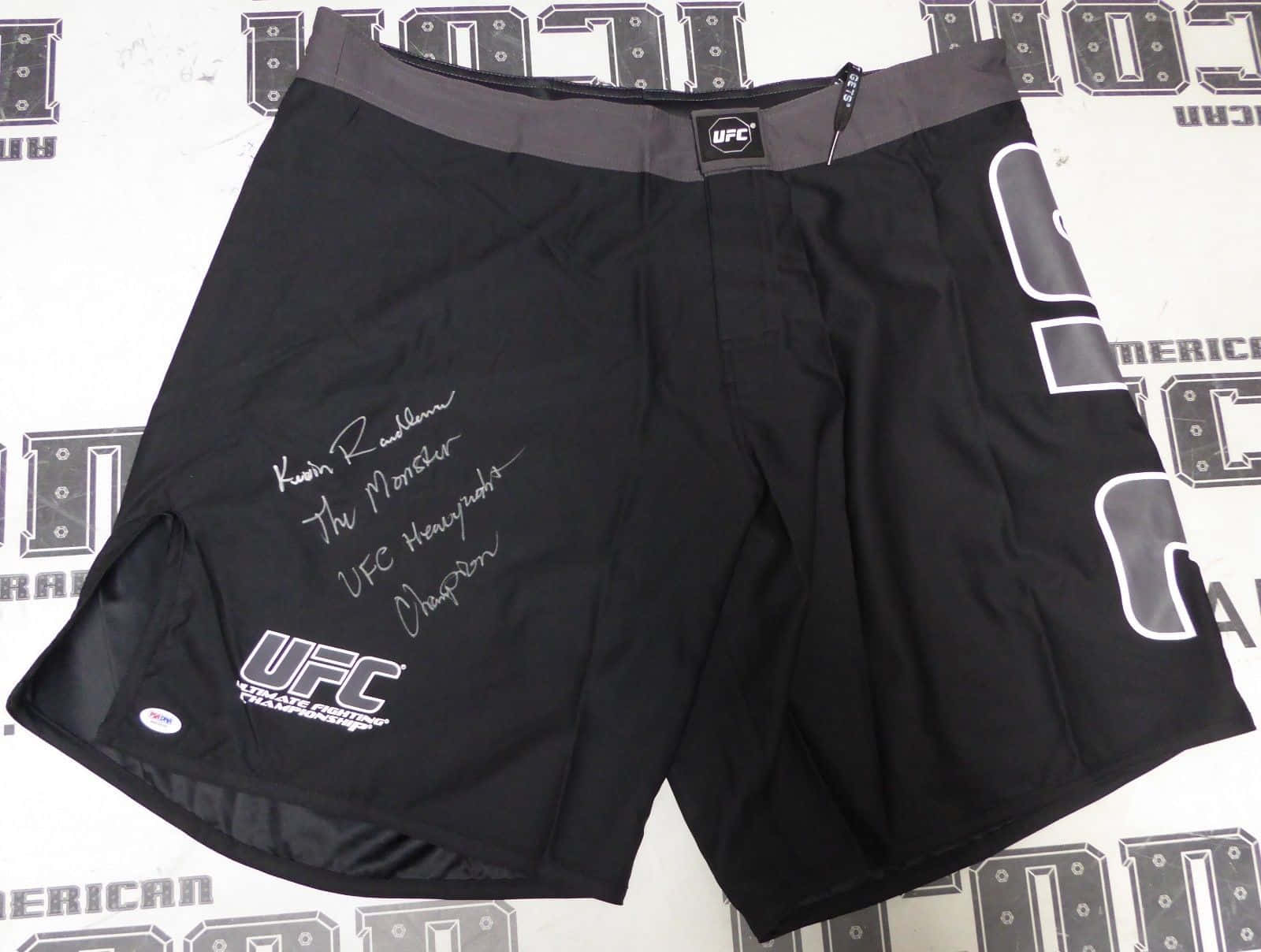 clothing 桌布 壁紙 — 黑色UFC格鬥短褲，印有Kevin Randleman的簽名和'The Monster'標題，展示在品牌背景上。