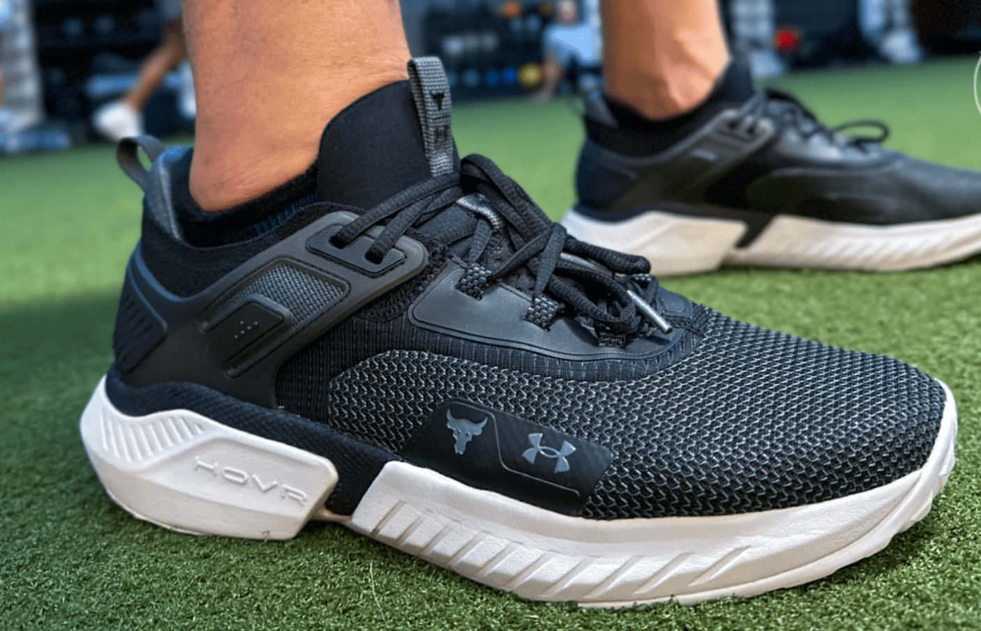 Under Armour 桌布 壁紙 — 黑色Under Armour HOVR運動鞋在綠色草地上的特寫，白色鞋底和紋理網眼鞋面。