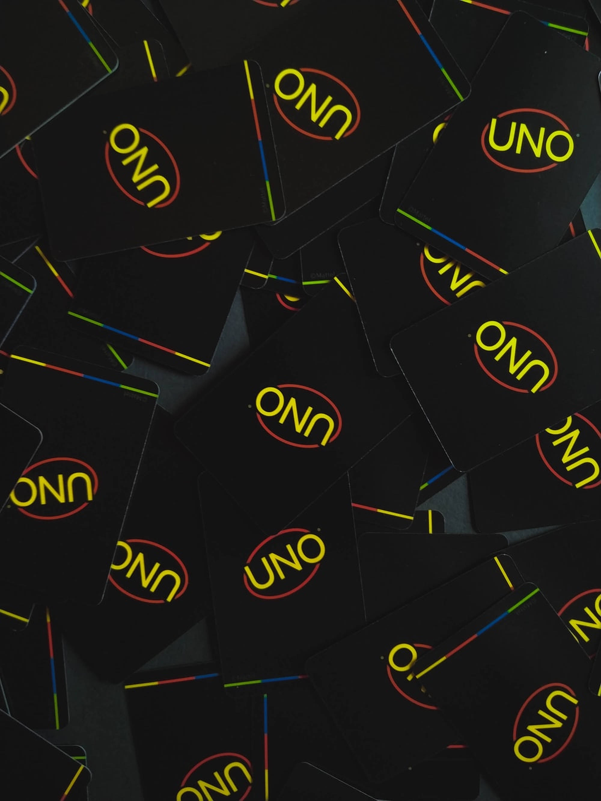Uno 桌布 壁紙 — 黑色UNO牌散落在深色表面上的特寫，帶有黃色標誌和彩色條紋。