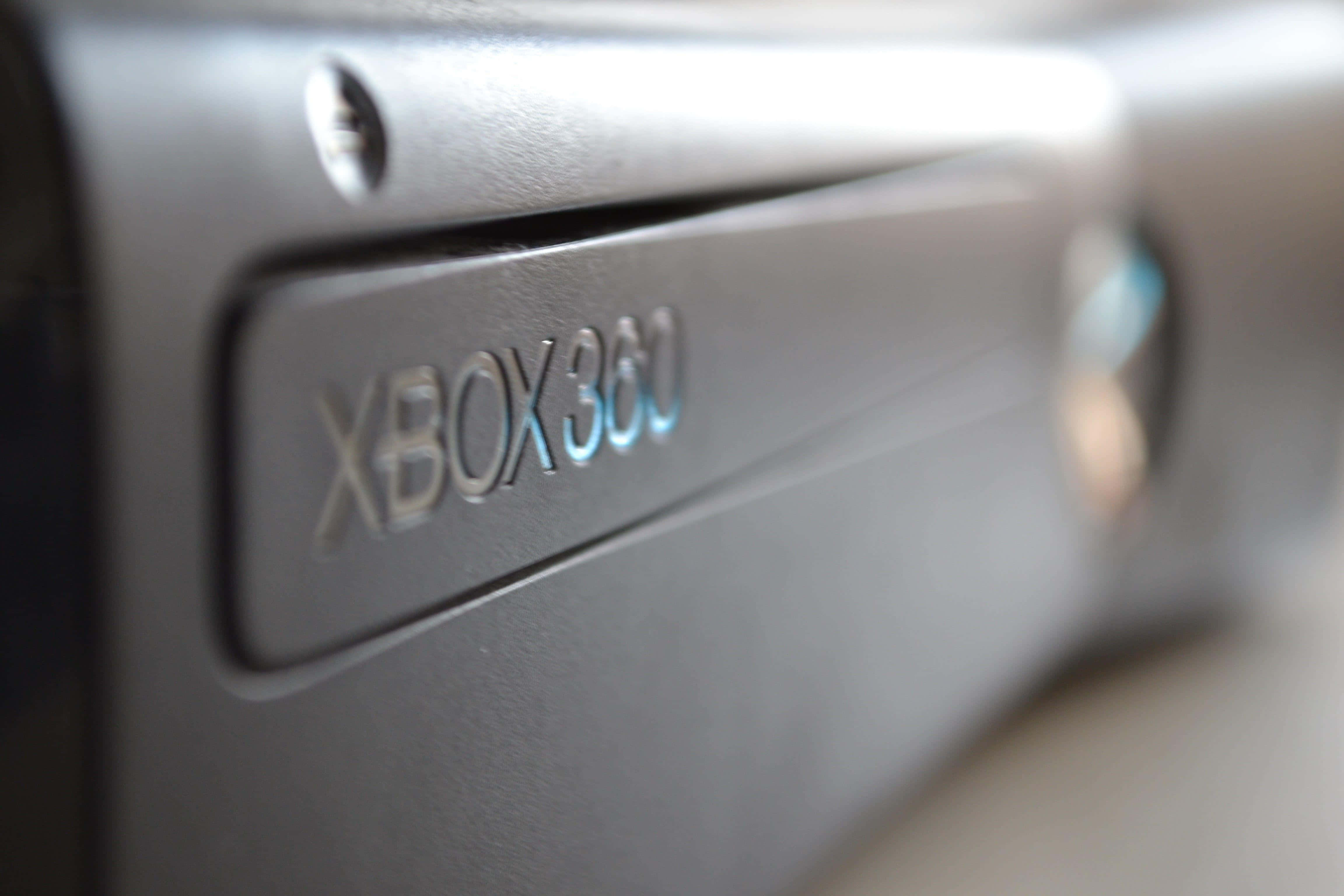 4K Gaming Consoles 桌布 壁紙 — 黑色Xbox 360主機特寫，設計時尚，帶有發光藍色標誌和淺景深效果。