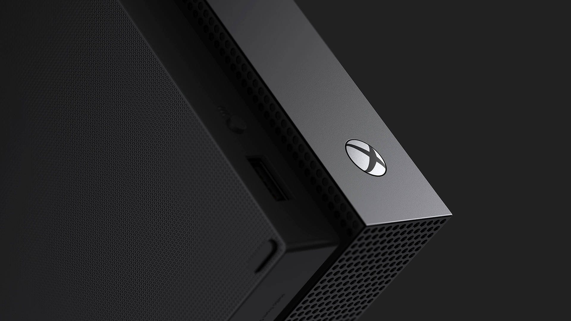 Xbox 桌布 壁紙 — 黑色Xbox主機角落的特寫，帶有穿孔通風口和發光標誌，背景為深色。