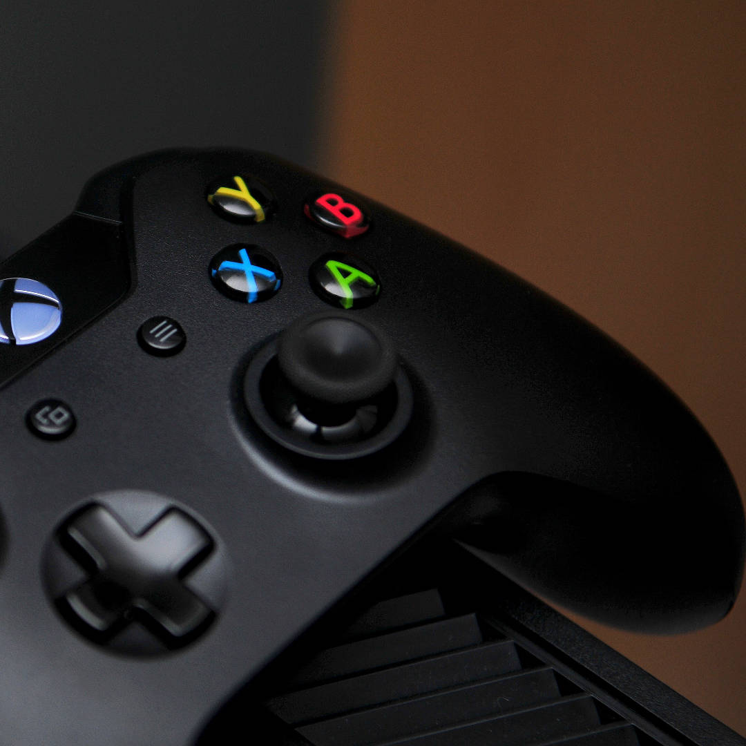 Xbox 桌布 壁紙 — 黑色Xbox手把特寫，帶有發光彩色按鈕，背景為溫暖的棕色。