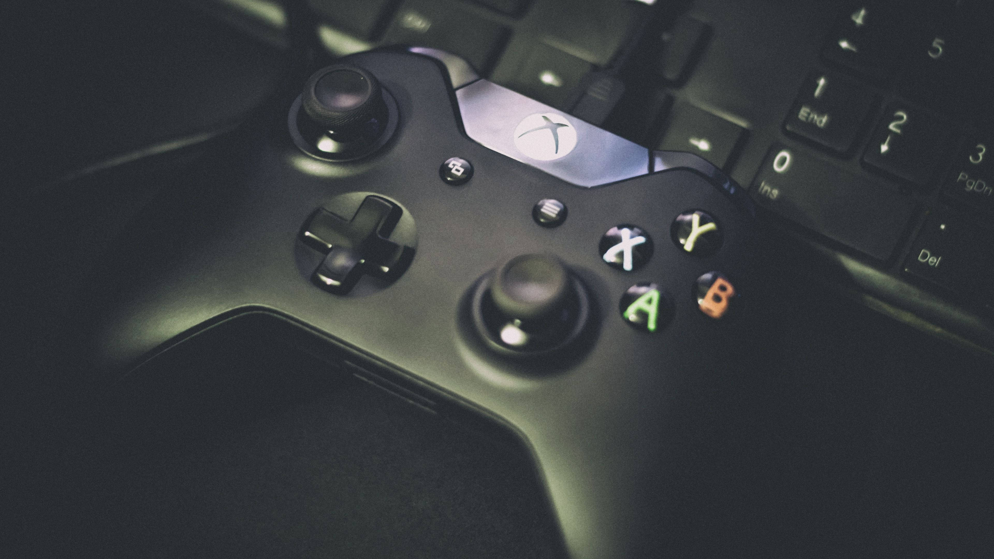 Xbox 桌布 壁紙 — 黑色Xbox控制器特寫，放在鍵盤上，按鈕發出柔和綠色光芒。