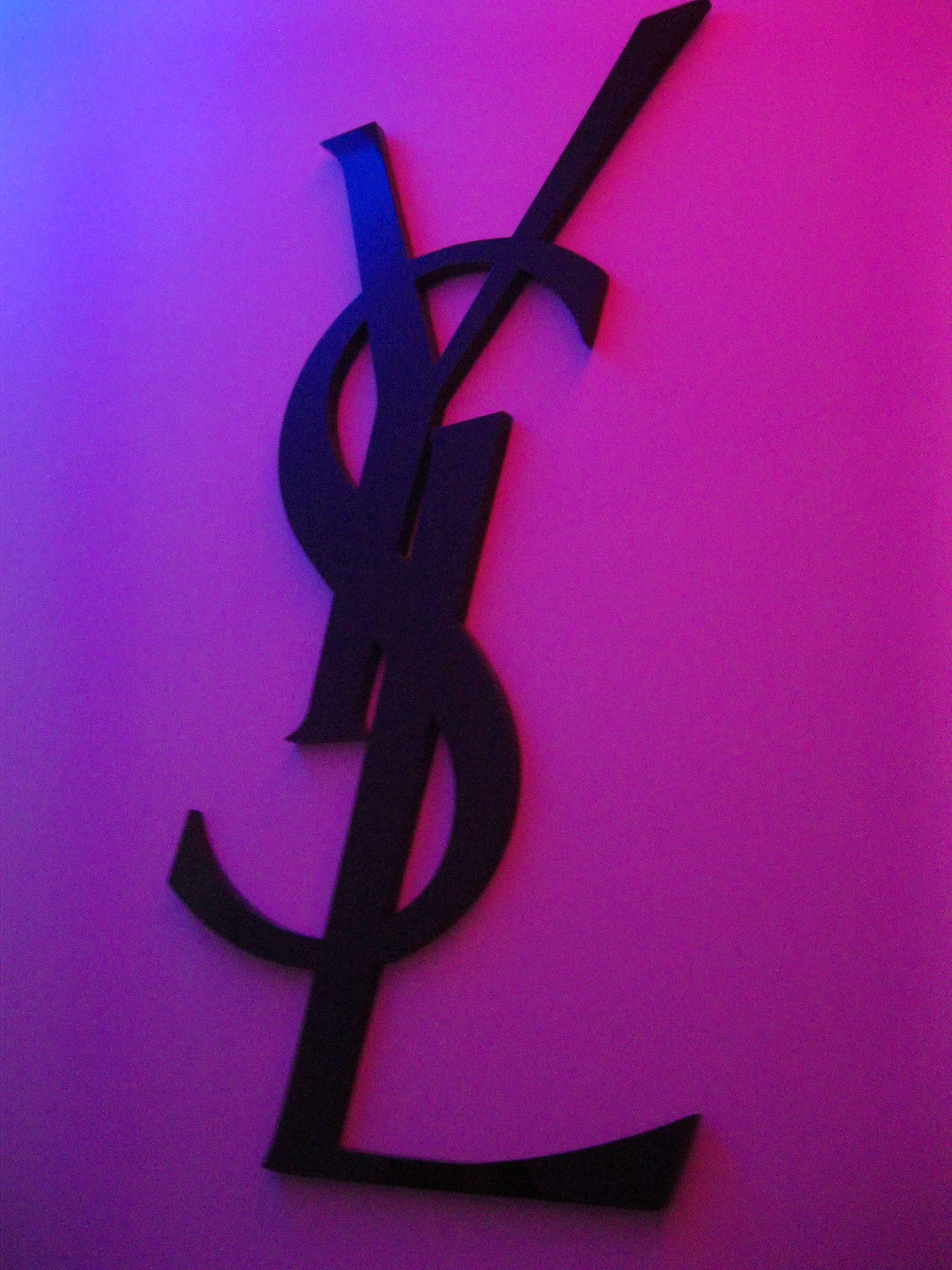YSL 桌布 壁紙 — 黑色YSL標誌鏤空在霓虹燈光下，襯托著充滿活力的紫色和粉紅色漸變牆。