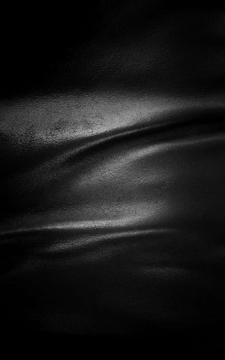 texture 桌布 壁紙 — 黑色亮面皮革的特寫，帶有細微皺摺和柔和高光，在定向照明下。