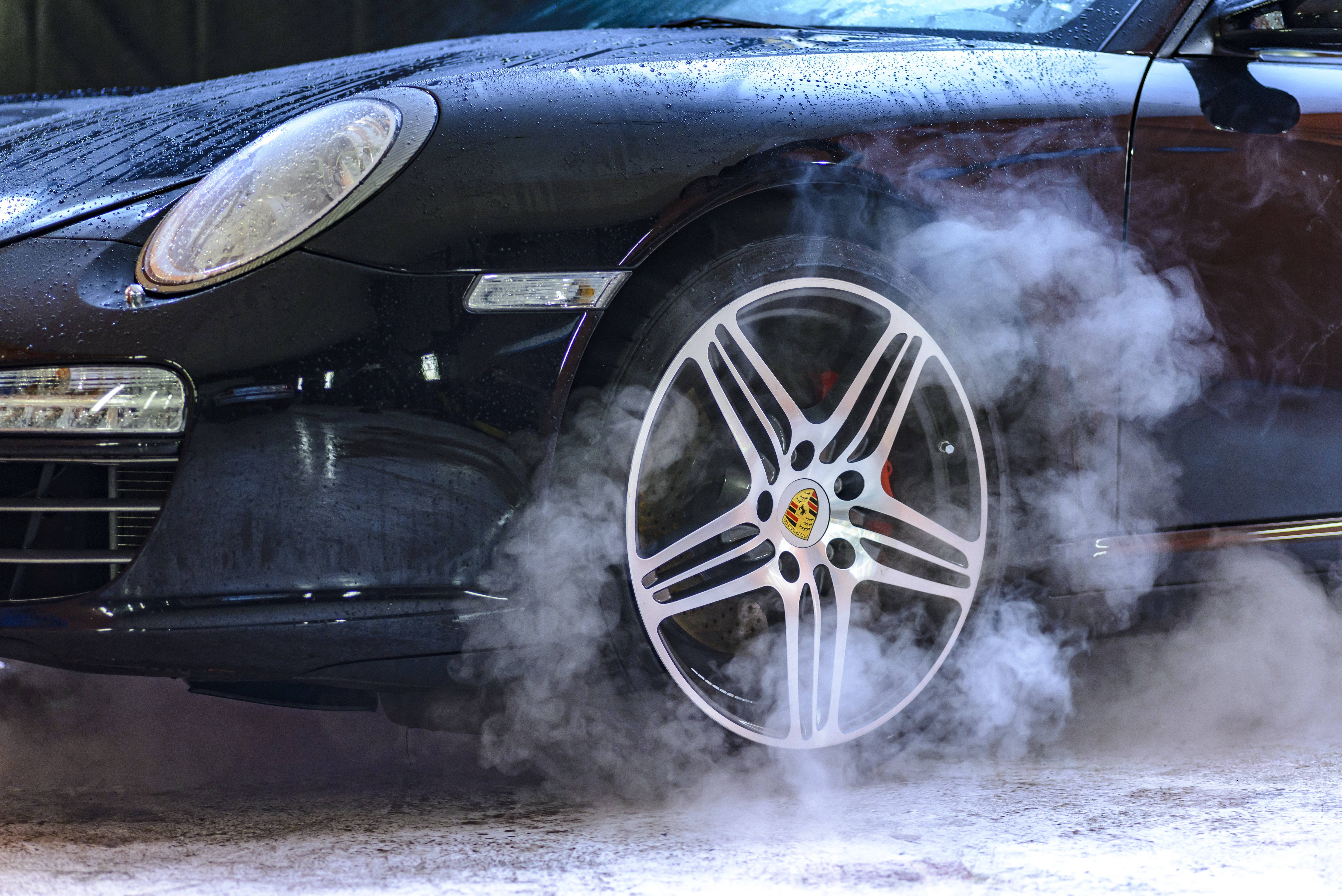 Cool Car 桌布 壁紙 — 黑色保時捷跑車的前輪在潮濕路面上冒著濃煙旋轉。