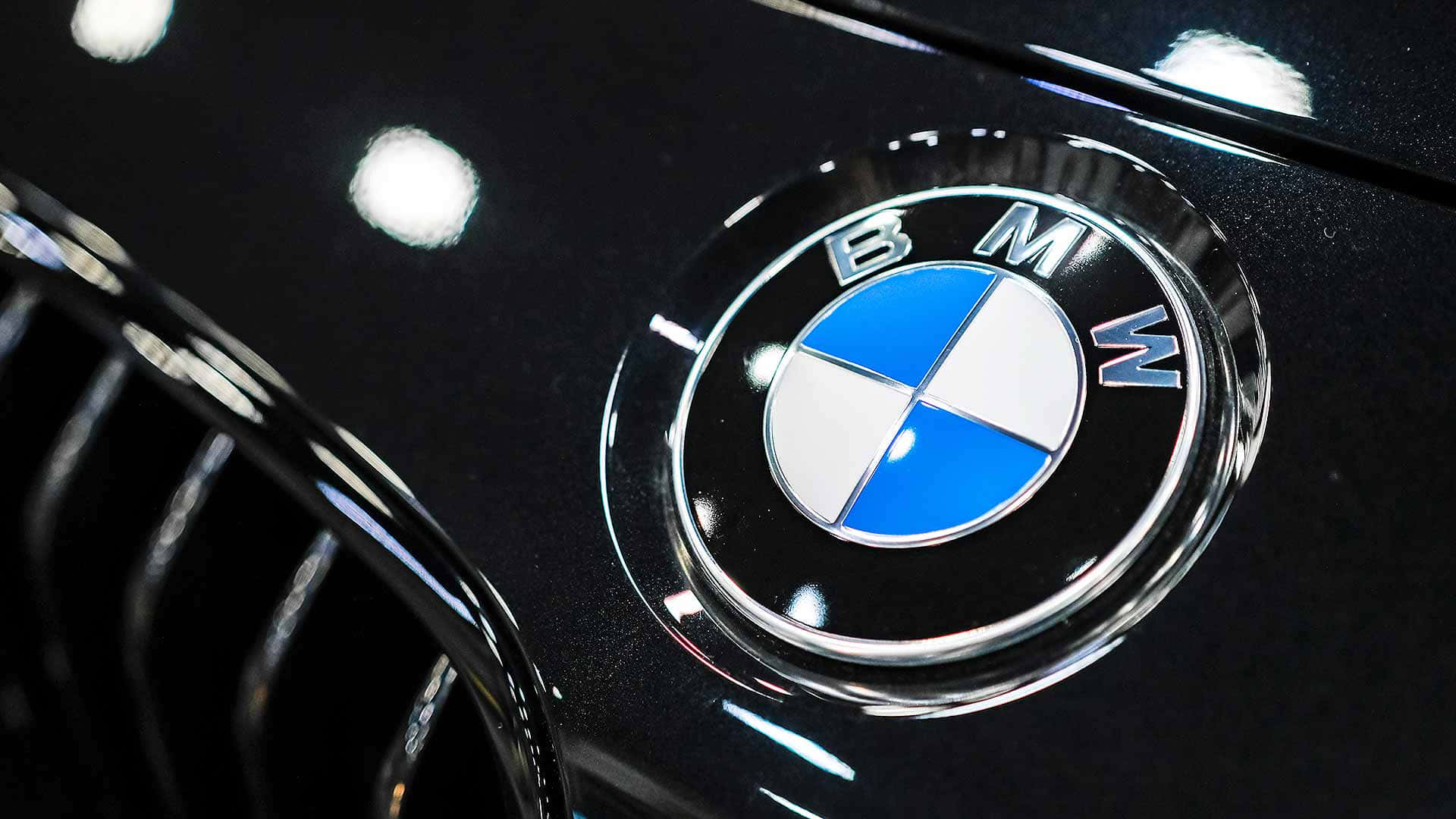 Bmw Logo 桌布 壁紙 — 黑色光面寶馬汽車引擎蓋的特寫，帶有標誌性的藍白圓形標誌、鍍鉻飾邊和反光。