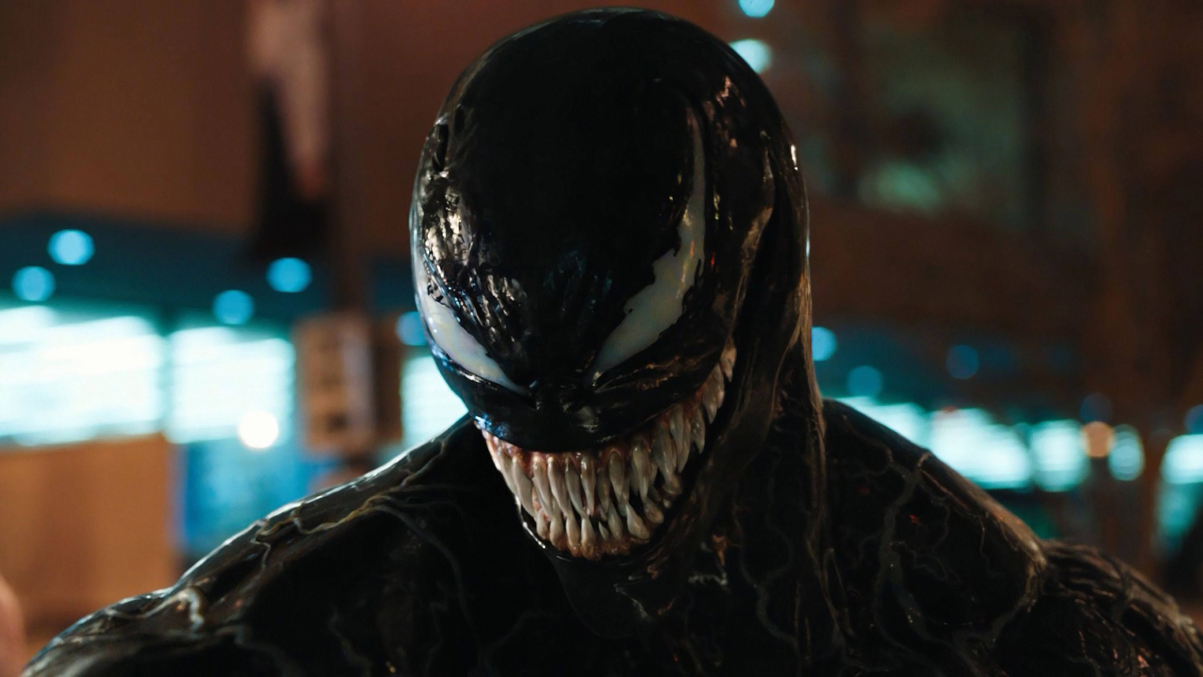 Venom Movie 桌布 壁紙 — 黑色共生體猛毒的特寫，帶有發光的白色眼睛和鋒利的牙齒，背景是模糊的城市夜景。