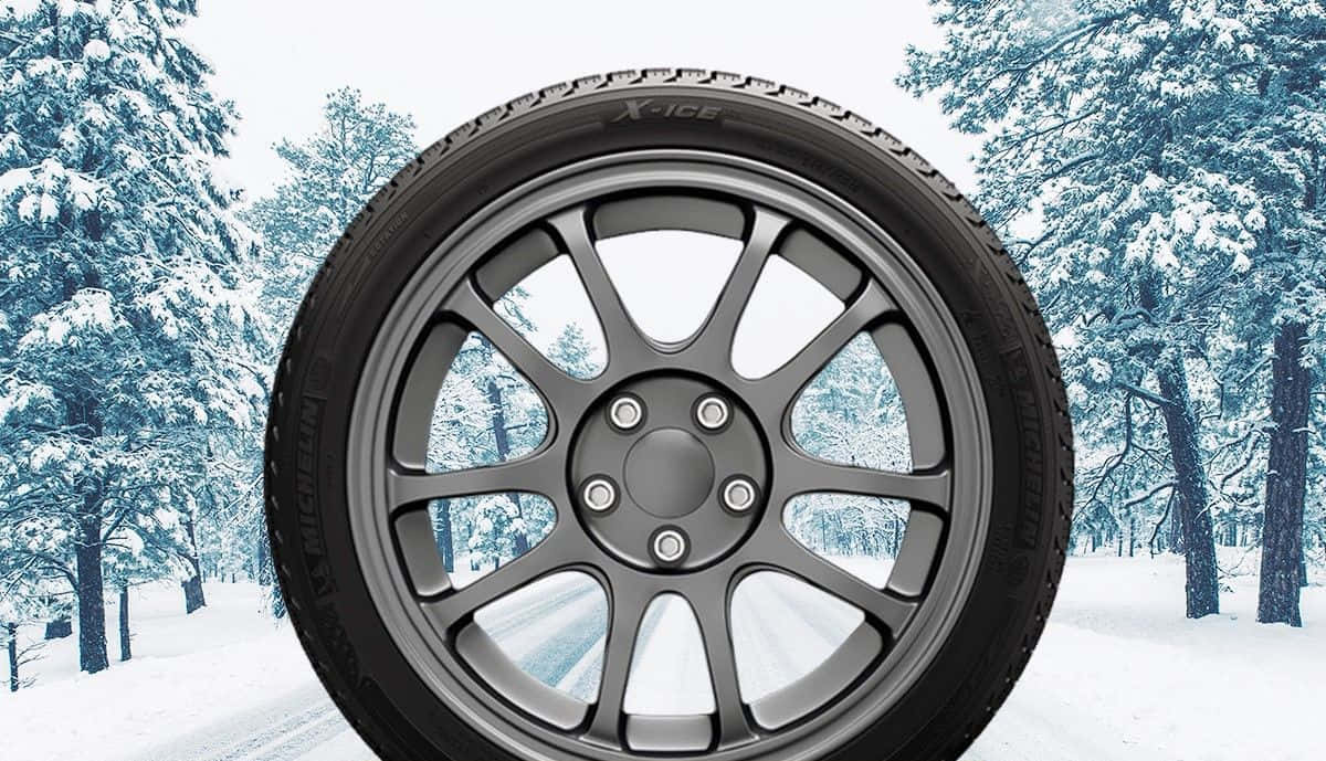 Winter Tires 桌布 壁紙 — 黑色冬季輪胎搭配銀色合金輪圈的近景，背景是雪覆蓋的森林。