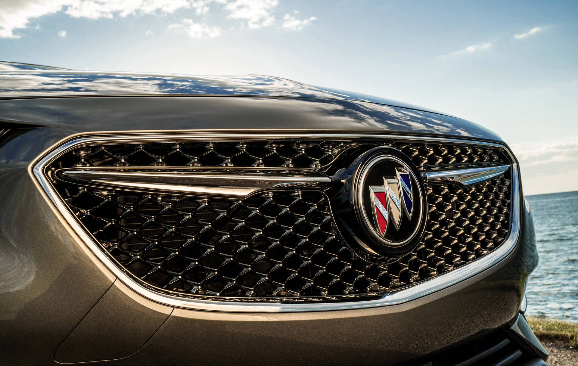 Buick 桌布 壁紙 — 黑色別克格柵特寫，帶有鍍鉻裝飾，反射明亮天空和海洋。