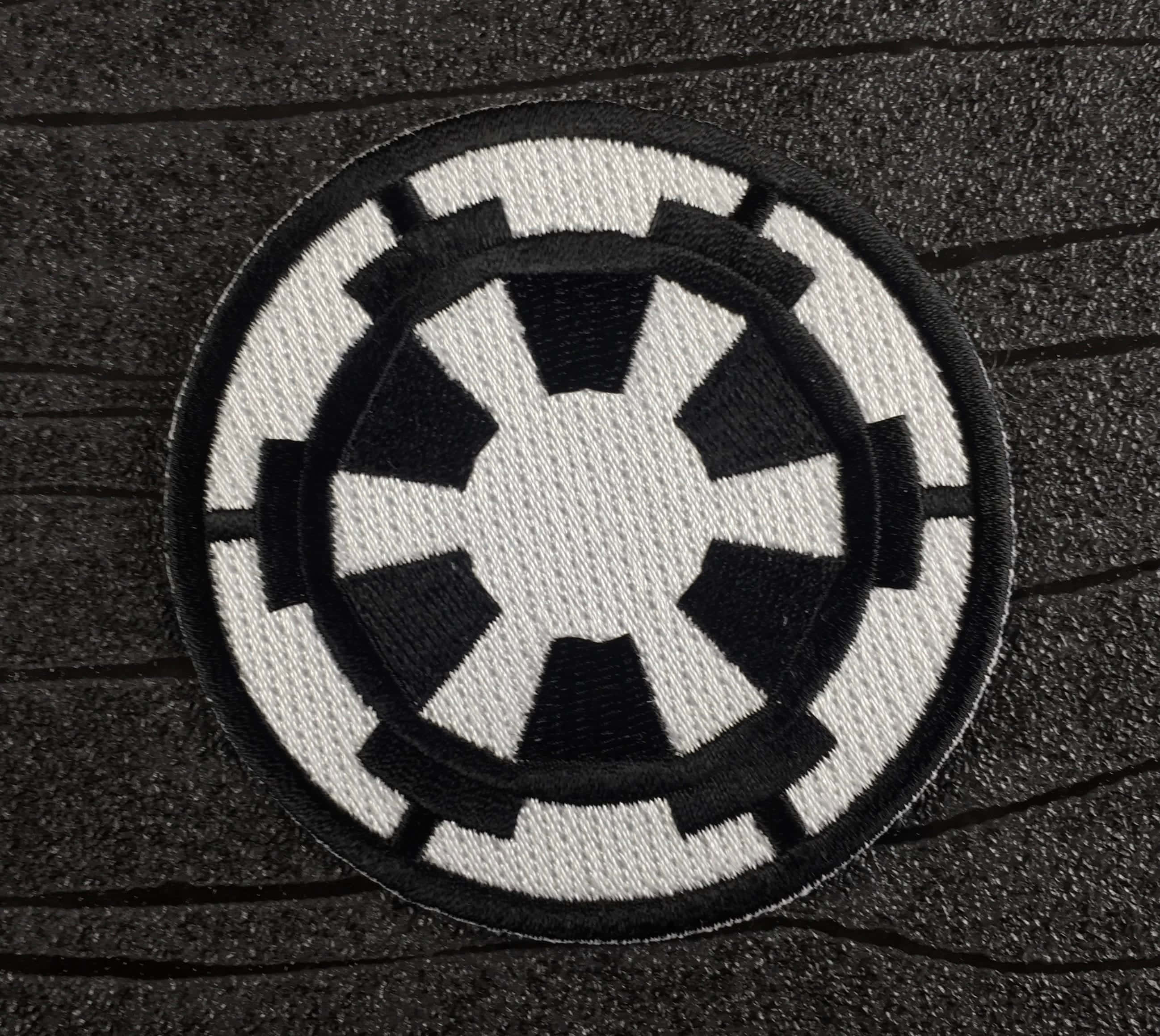 桌布 壁紙 — 黑色和白色刺繡的帝國徽章補丁在深色紋理表面上的特寫。