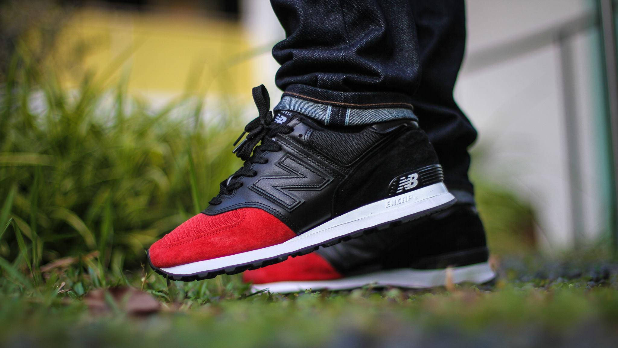 New 桌布 壁紙 — 黑色和紅色 New Balance 運動鞋在草地上，搭配牛仔褲和模糊的黃色牆壁背景的特寫。