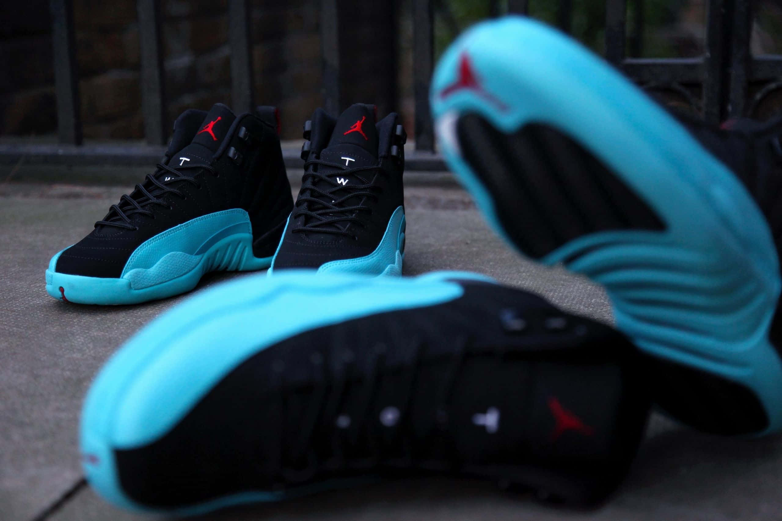 Jordan球鞋 桌布 壁紙 — 黑色和藍綠色的Jordan 12運動鞋帶有紅色標誌，排列在石頭庭院中，配有鍛鐵圍欄，在柔和日光下。