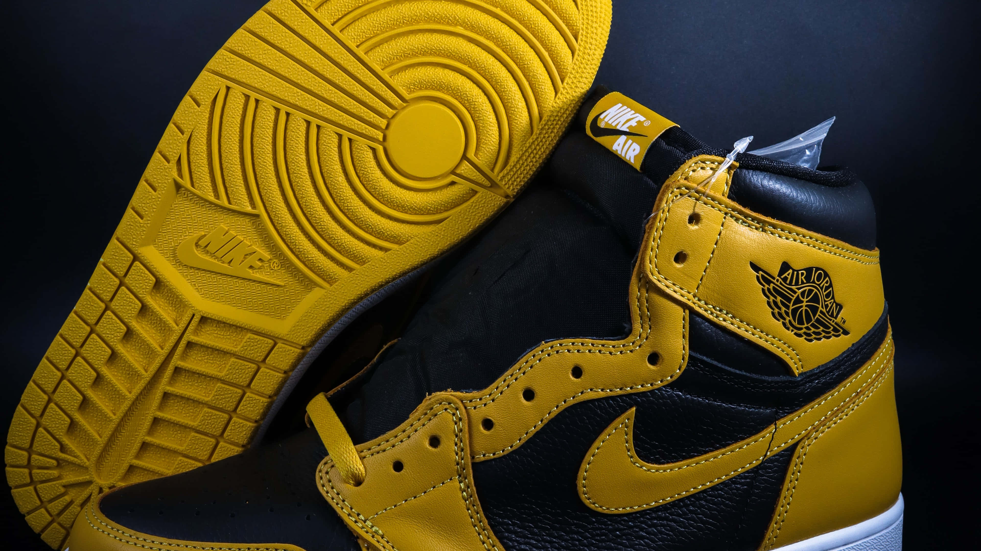 桌布 壁紙 — 黑色和金色Air Jordan 1運動鞋的特寫，鞋底抬起，在深色背景下展示細緻紋理。