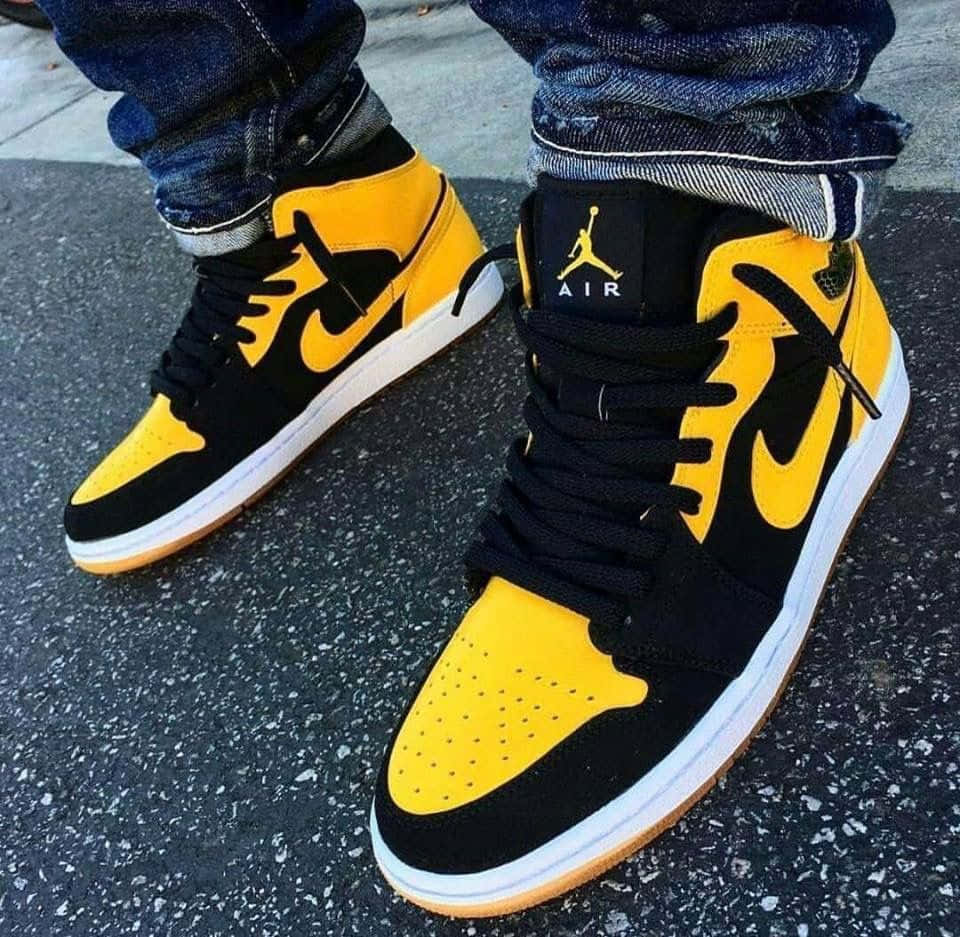 Yellow Jordan 桌布 壁紙 — 黑色和黃色Jordan 1運動鞋特寫，搭配橡膠鞋底，穿著捲邊牛仔褲在柏油路上。