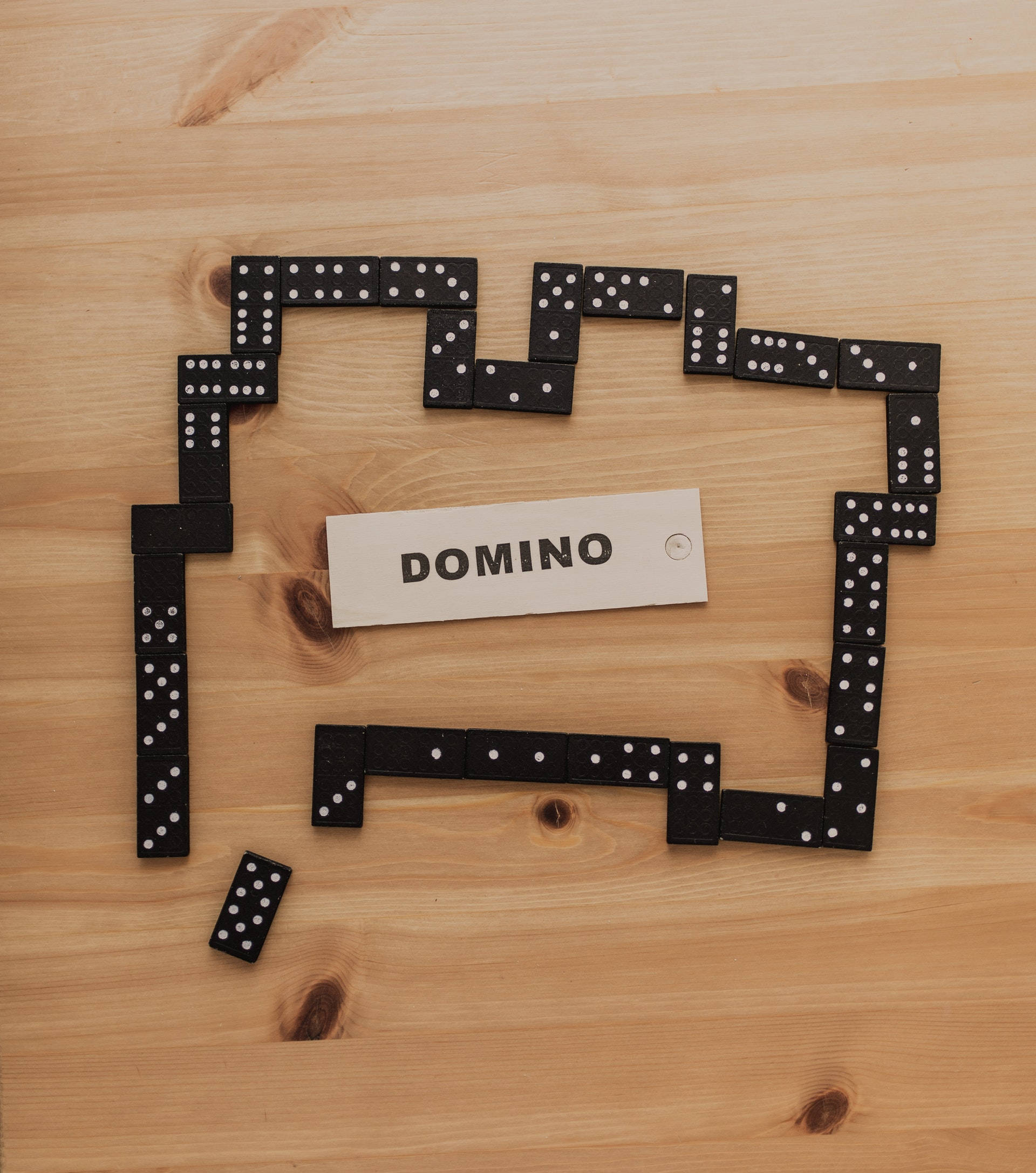 Domino 桌布 壁紙 — 黑色多米諾骨牌在淺色木頭上排列成矩形框架，中間有「DOMINO」標籤。