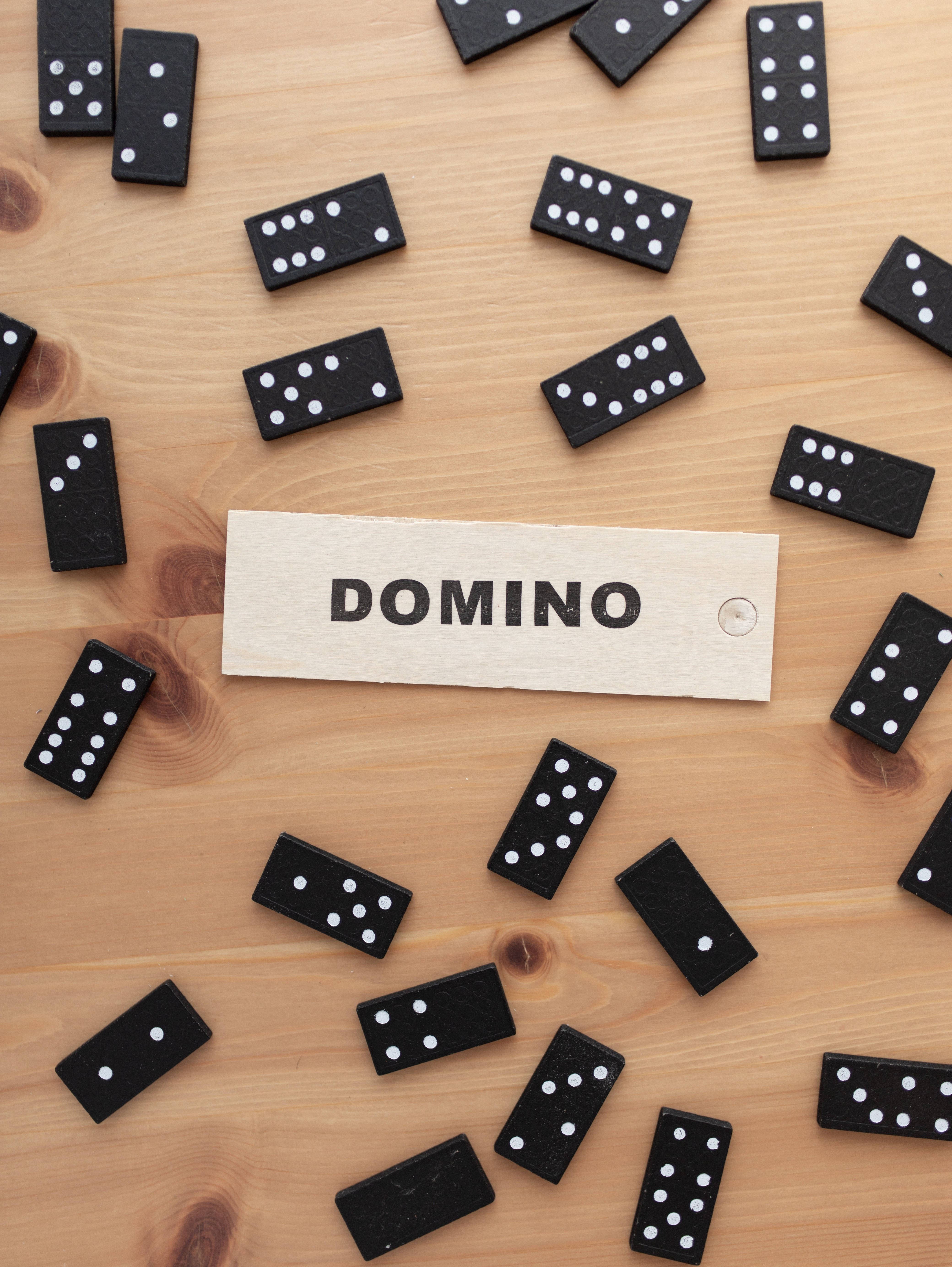 dominos 桌布 壁紙 — 黑色多米諾骨牌帶有白色點點，散落在淺色木質表面上，圍繞著一個寫有DOMINO的木牌。