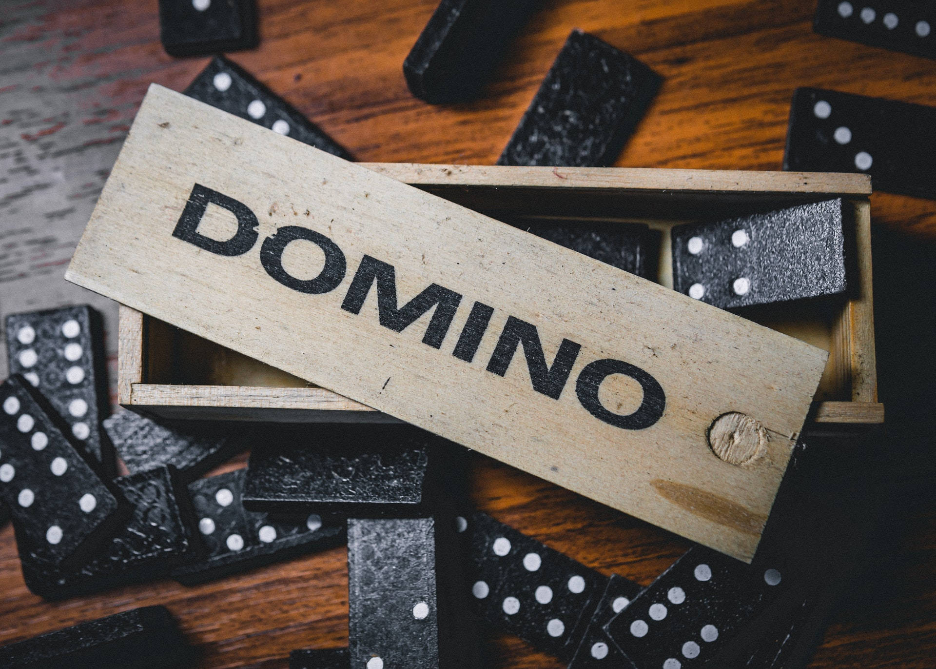 Domino 桌布 壁紙 — 黑色多米諾骨牌從一個標有DOMINO的木盒中灑落在暖色調的木質表面上。
