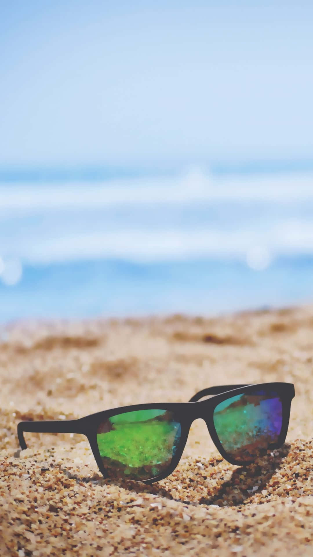 Android Summer 桌布 壁紙 — 黑色太陽眼鏡放在金色沙灘上，背景是模糊的海浪和藍天。