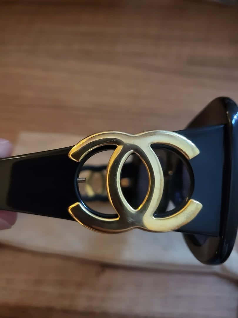香奈兒標誌 桌布 壁紙 — 黑色太陽眼鏡特寫，帶有金色交錯CC標誌，置於木質表面上。