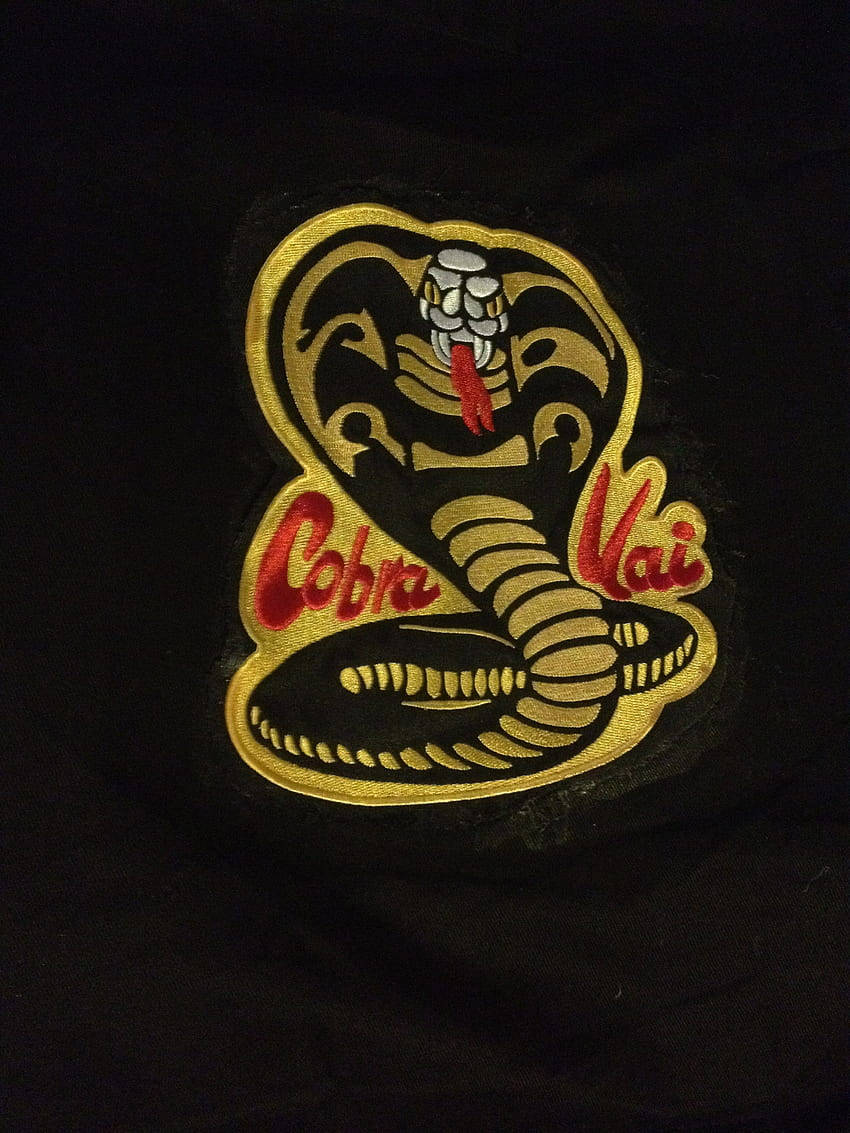 Cobra Kai Phone 桌布 壁紙 — 黑色布料上金色和紅色刺繡的眼鏡蛇補丁特寫，帶有 'Cobra Vai' 文字。