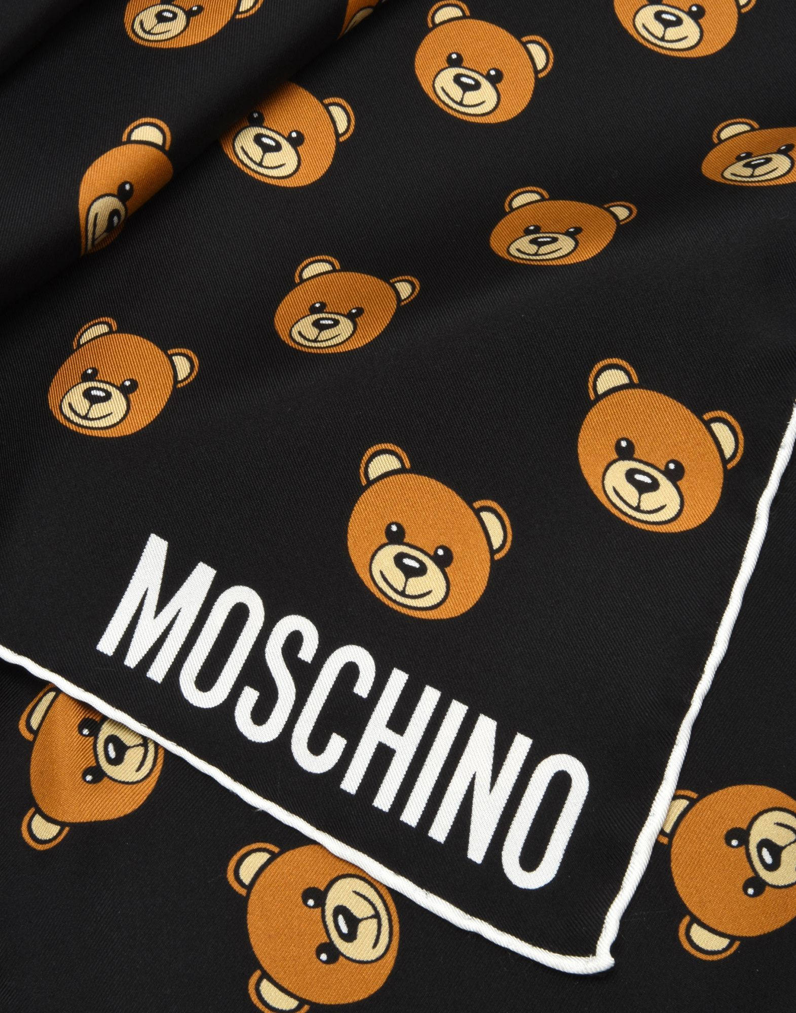 moschino 桌布 壁紙 — 黑色布料圍巾的特寫，帶有重複的橙色泰迪熊臉和粗體白色MOSCHINO品牌標誌。