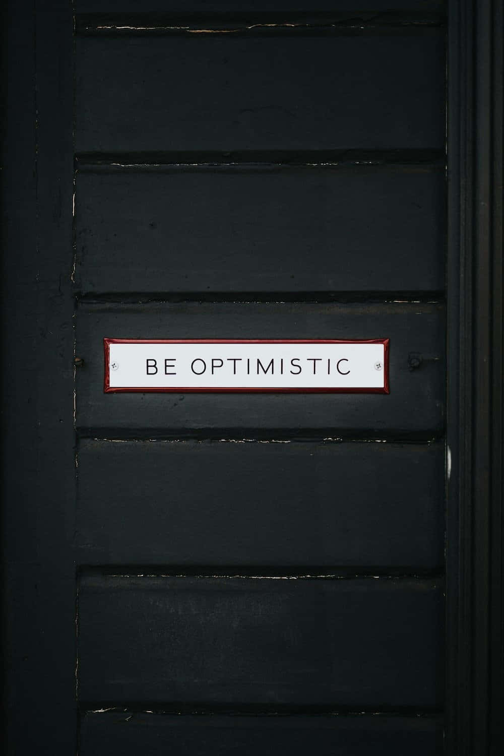 Motivational Quotes 桌布 壁紙 — 黑色木門的特寫，上面有一個白色標牌，以粗體字寫著「BE OPTIMISTIC」。
