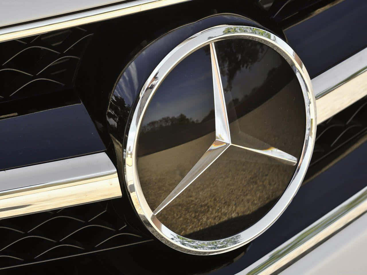 Mercedes Benz Logo 桌布 壁紙 — 黑色格柵上閃亮鍍鉻賓士標誌的特寫，反射樹木和天空。