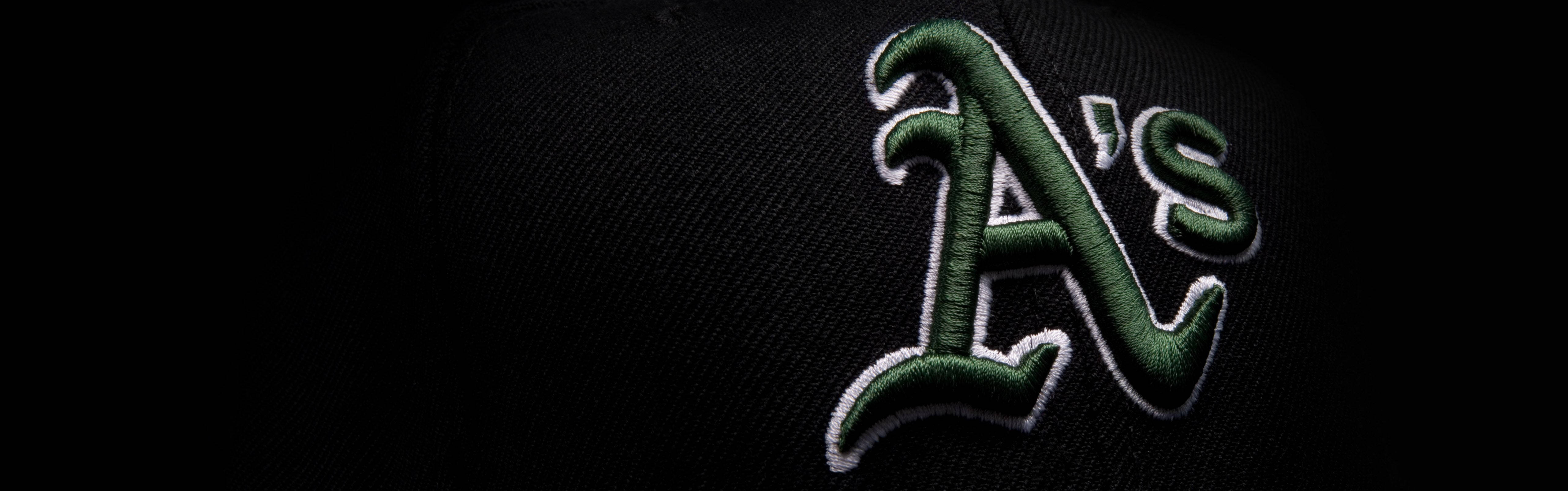 Athletics 桌布 壁紙 — 黑色棒球帽的特寫，帽上繡有綠色和白色的A's標誌，背景為深色。