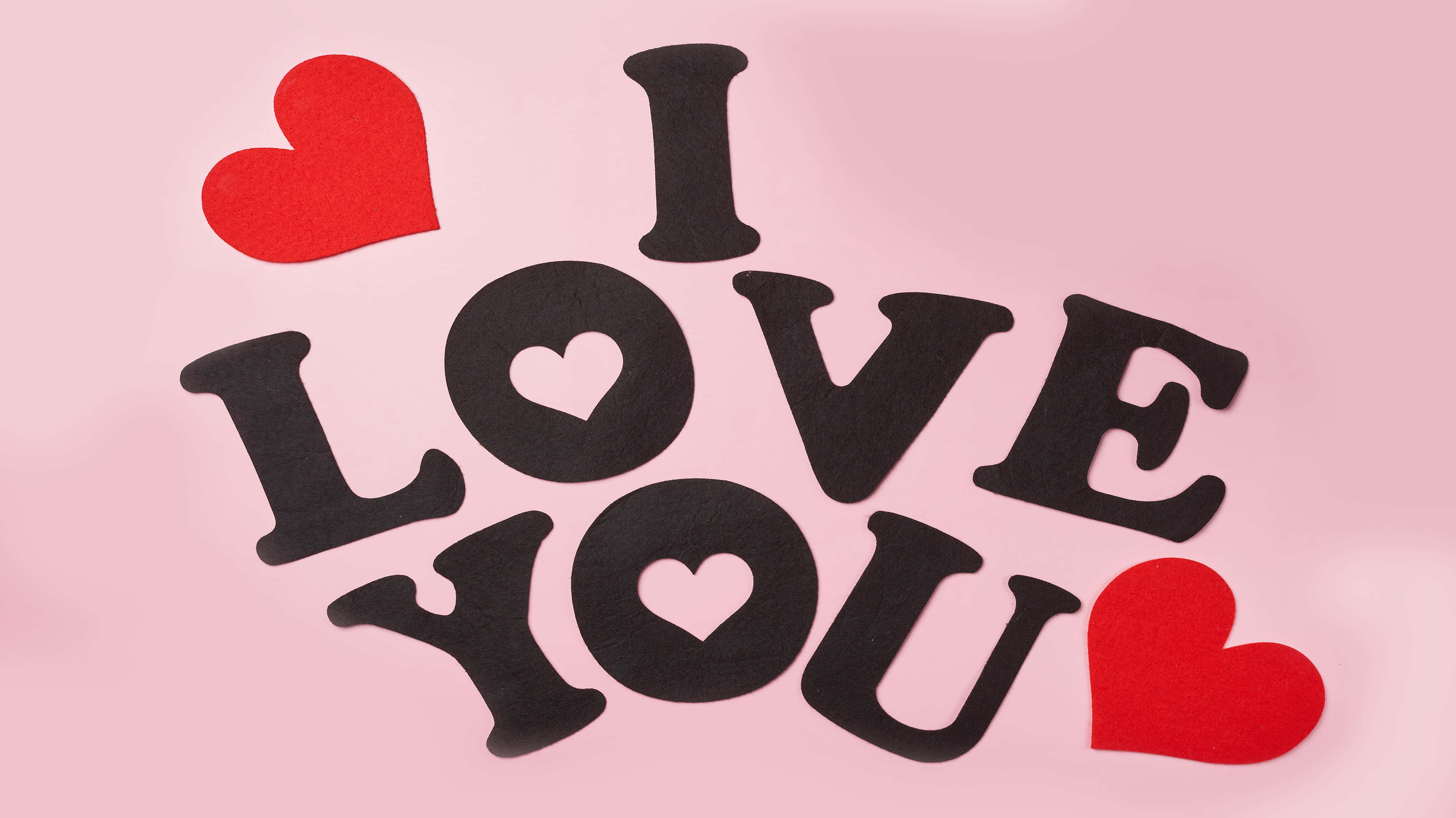 3840x2160 動態圖片 桌布 壁紙 — 黑色氈字拼出 I LOVE YOU，配上紅色心形，在柔和的粉紅色背景上。
