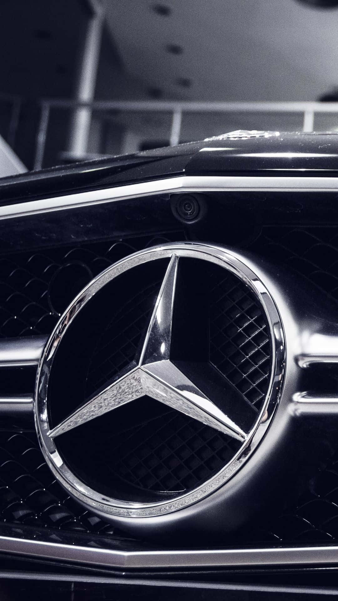 Mercedes 桌布 壁紙 — 黑色汽車格柵上閃閃發光的賓士星形標誌特寫，帶有鍍鉻裝飾和模糊背景。