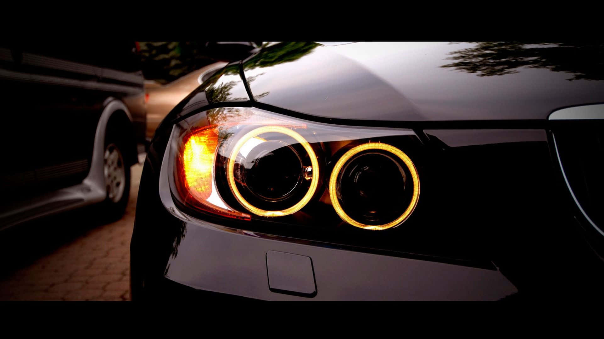 BMW 動圖 桌布 壁紙 — 黑色汽車發光光環頭燈在低光下的特寫，背景有模糊的卡車。
