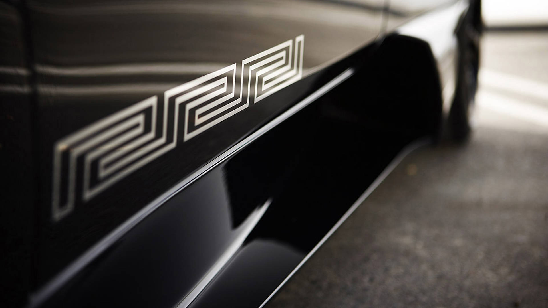 Logo Design 桌布 壁紙 — 黑色流線型汽車側面板的特寫，帶有醒目的白色幾何「222」標誌，在光澤漆面上有銳利反射。