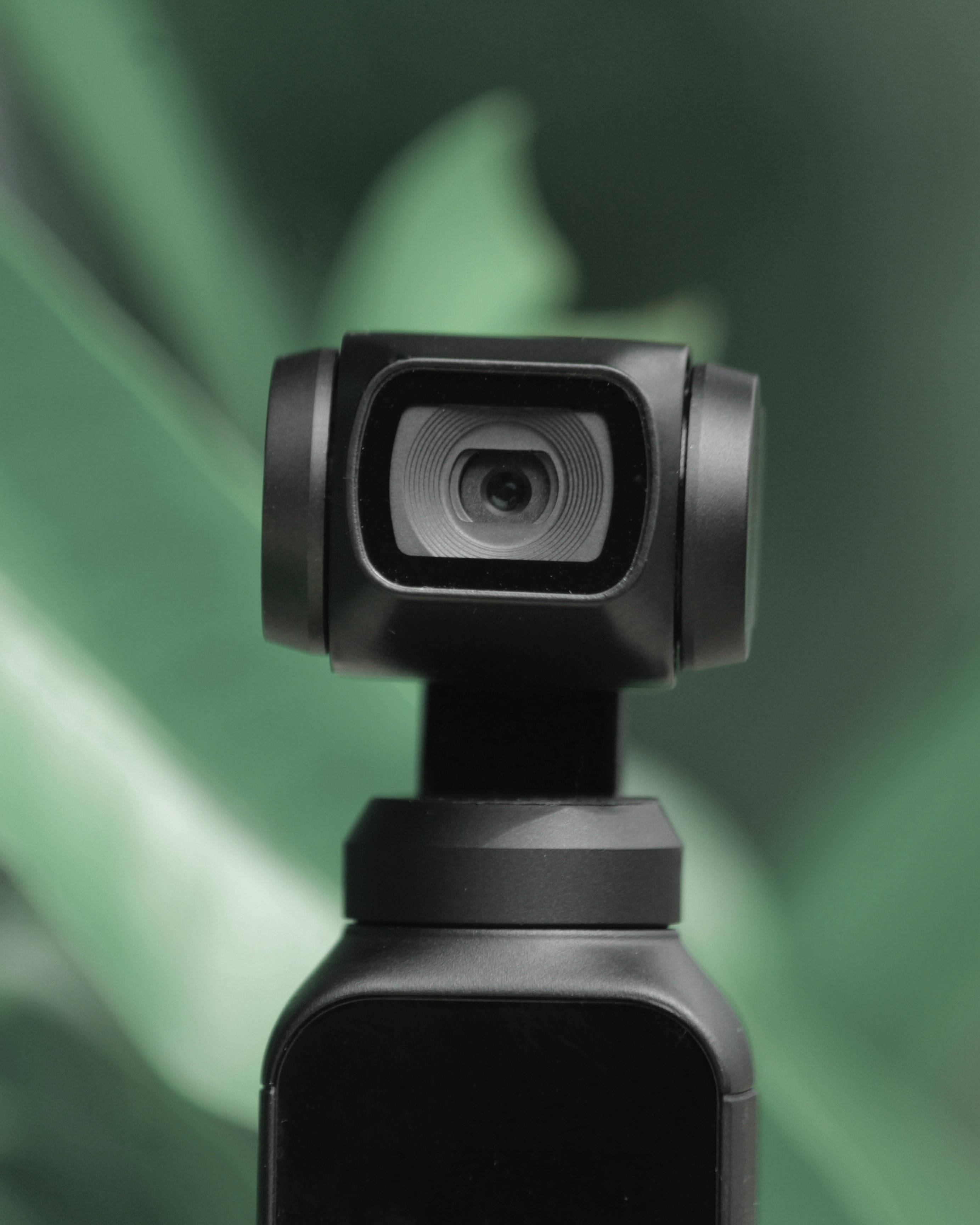 Webcam 桌布 壁紙 — 黑色流線型運動相機特寫，背景為柔和綠色葉片。