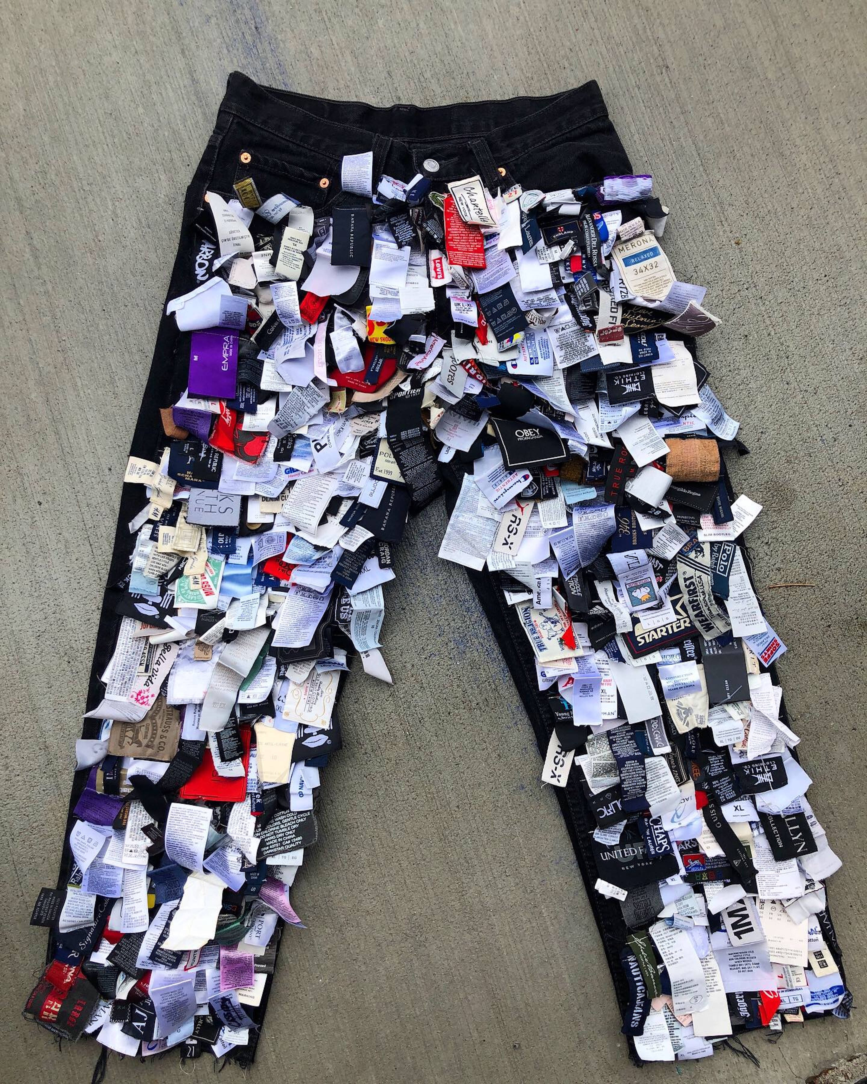 Trendy 桌布 壁紙 — 黑色牛仔褲上覆蓋著色彩繽紛的服裝標籤的混亂拼貼，平放在灰色混凝土表面上。