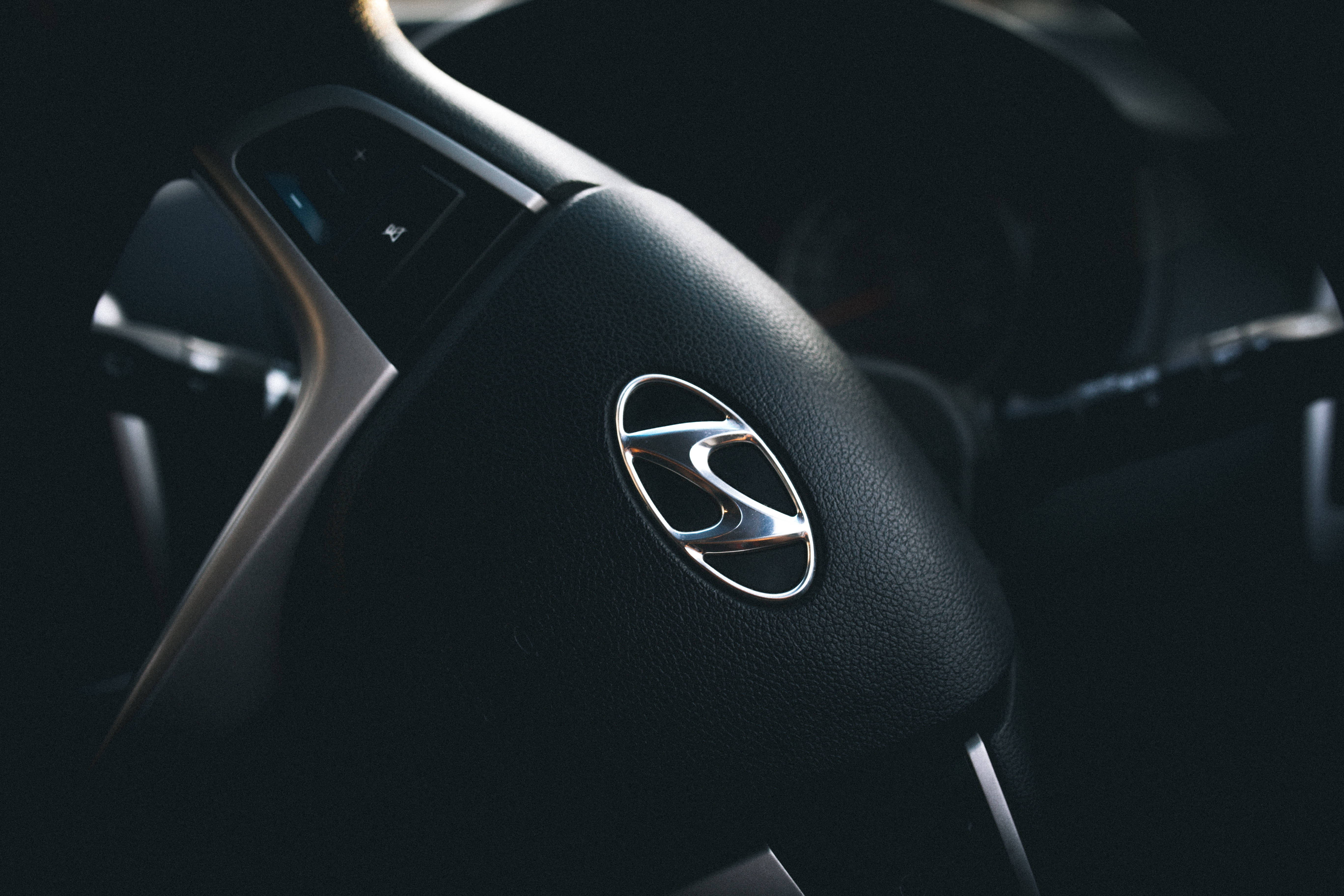 Hyundai 桌布 壁紙 — 黑色現代汽車方向盤特寫，帶有鍍鉻標誌，在戲劇性的低調燈光下。