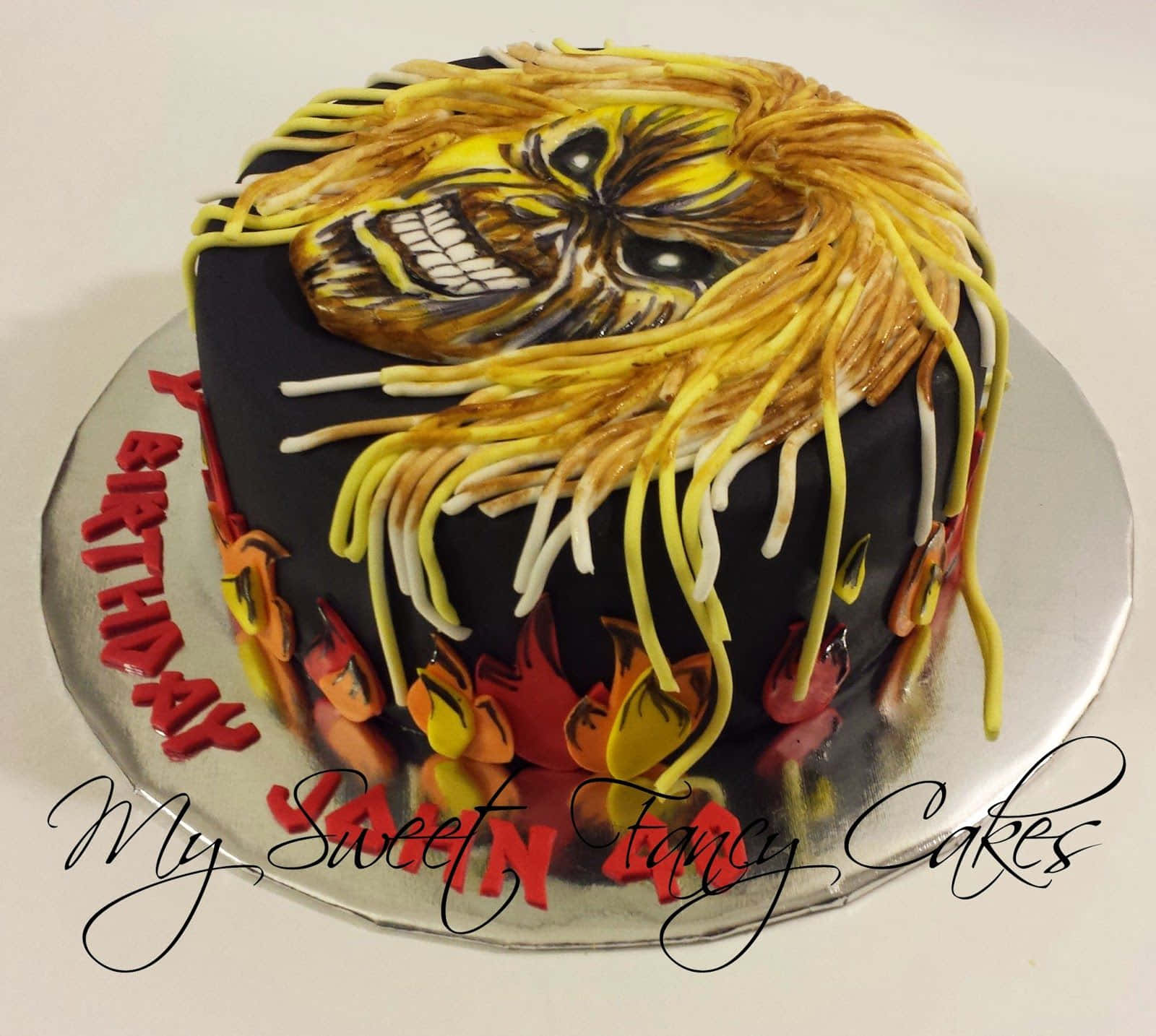 Ugly Cake 桌布 壁紙 — 黑色生日蛋糕，上面有詳細的鐵娘子艾迪臉和滴落的黃色糖霜頭髮。