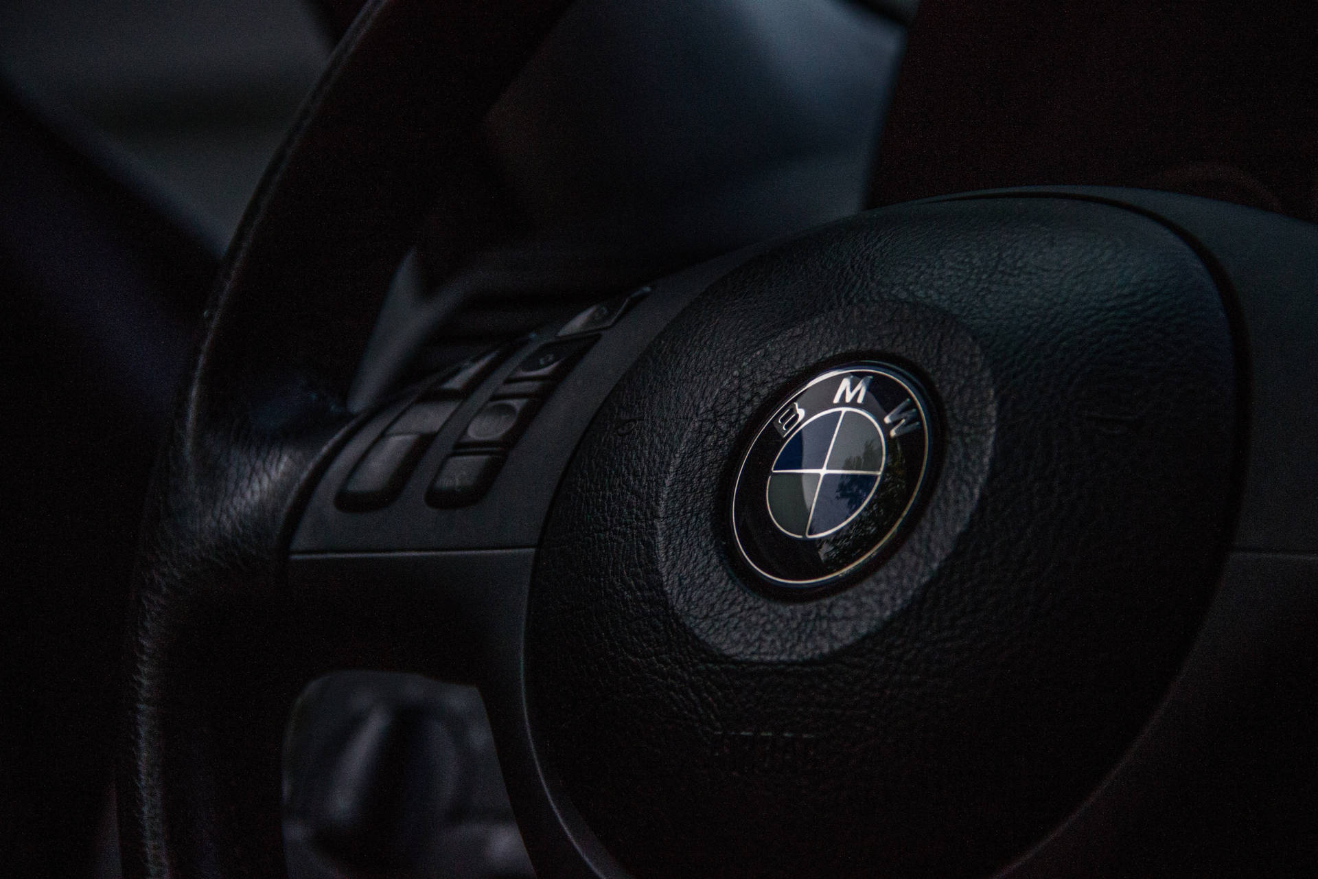 BMW 動圖 桌布 壁紙 — 黑色皮革BMW方向盤特寫，標誌在昏暗光線下發光。