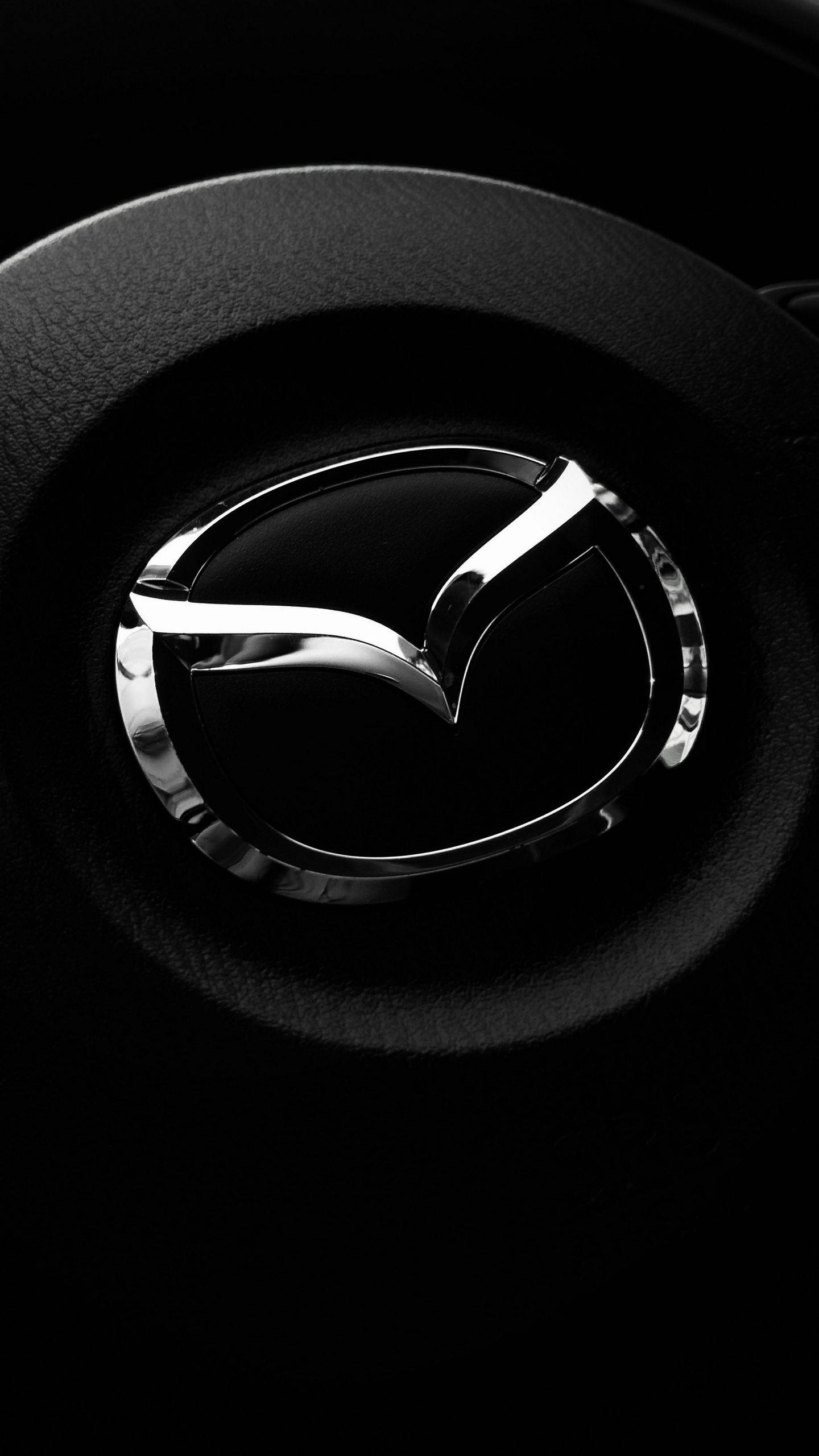 Mazda 桌布 壁紙 — 黑色皮革方向盤中央的閃亮鍍鉻Mazda標誌特寫。