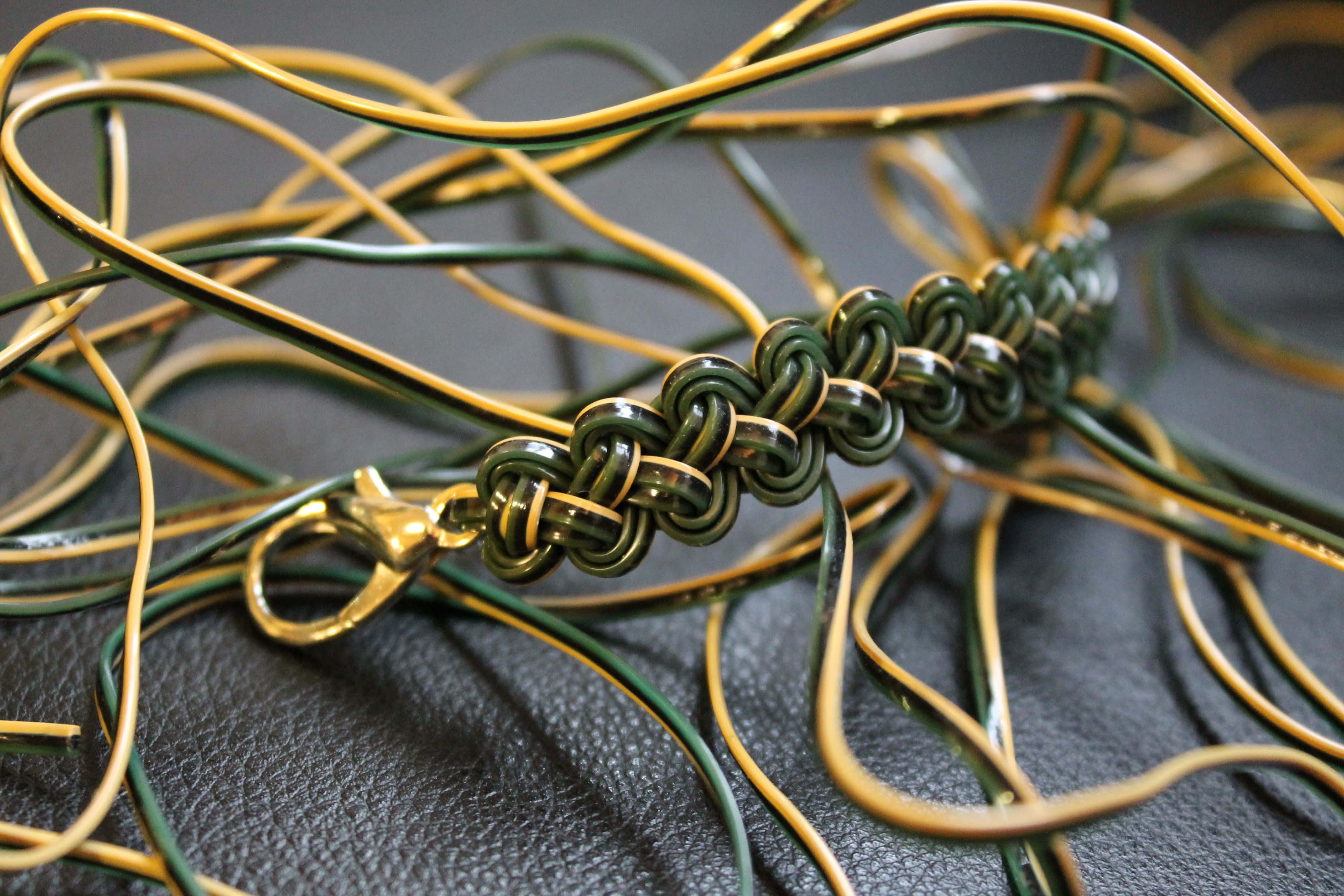 Butterfly Stitch 桌布 壁紙 — 黑色皮革表面上深綠色和金色編織繩手鍊及金色扣環的特寫。
