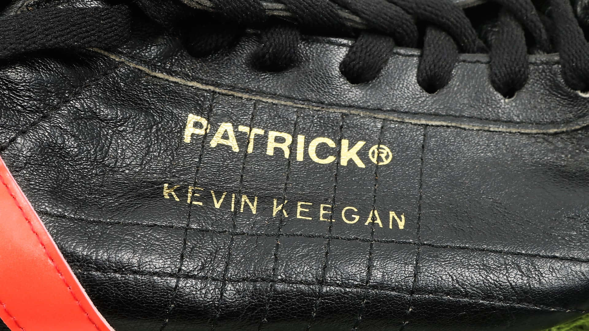 鞋子 桌布 壁紙 — 黑色皮革足球靴特寫，帶有金色 'PATRICK KEVIN KEEGAN' 品牌標誌和紅色點綴。