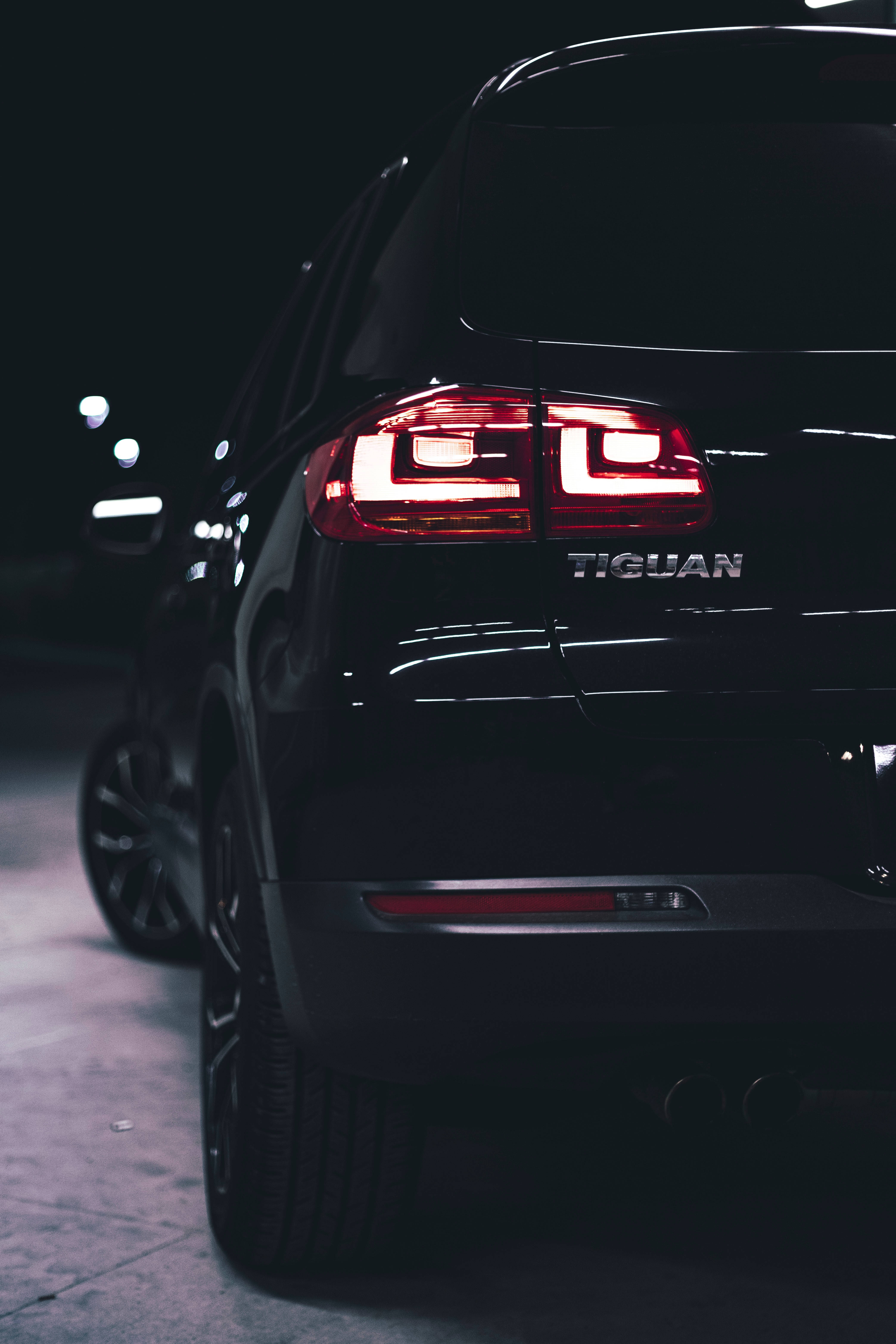 福斯汽車 桌布 壁紙 — 黑色福斯 Volkswagen Tiguan SUV 在夜間發出紅色光芒的尾燈特寫，背景是模糊的城市燈光。