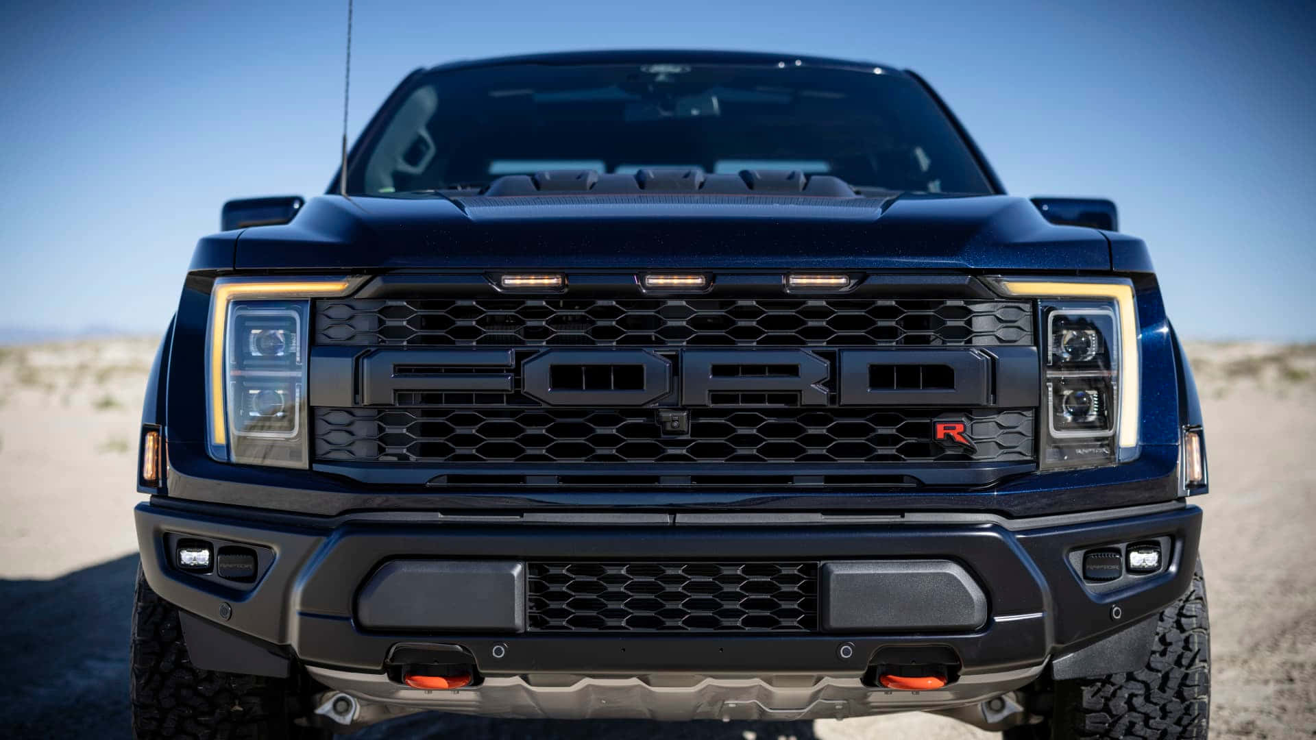Ford Logo 桌布 壁紙 — 黑色福特 Raptor 卡車在明亮沙漠陽光下，其侵略性前格柵和頭燈的特寫。