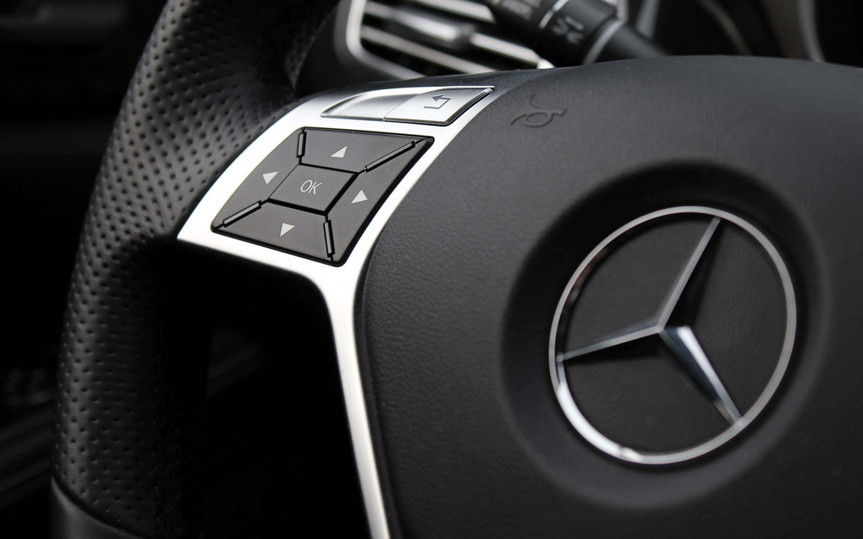 Mercedes Benz Logo 桌布 壁紙 — 黑色穿孔皮革賓士方向盤特寫，帶有銀色控制按鈕和標誌性三芒星標誌。