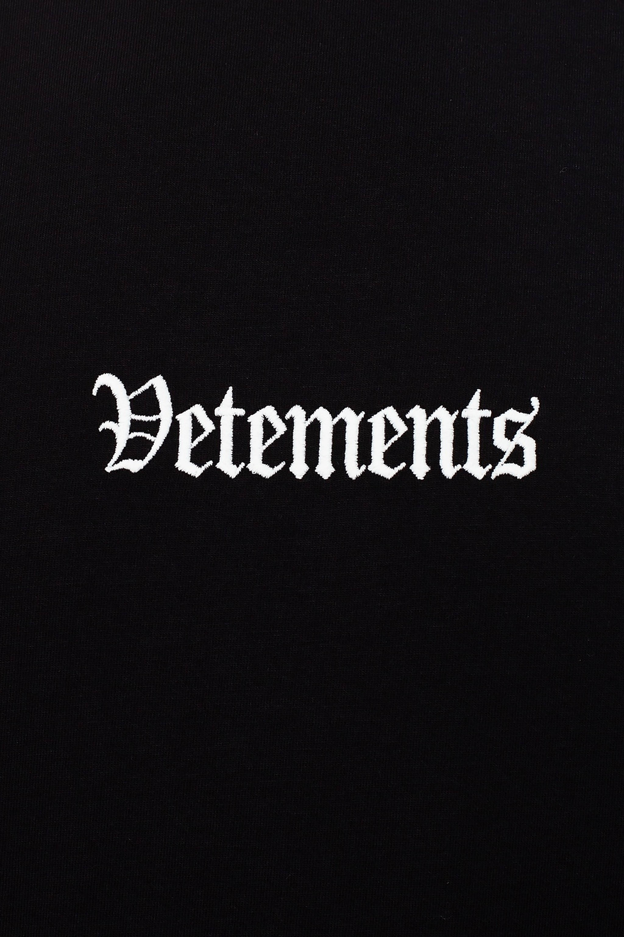Vetements 桌布 壁紙 — 黑色紋理布料上白色哥德式刺繡 'Vetements' 標誌的特寫。
