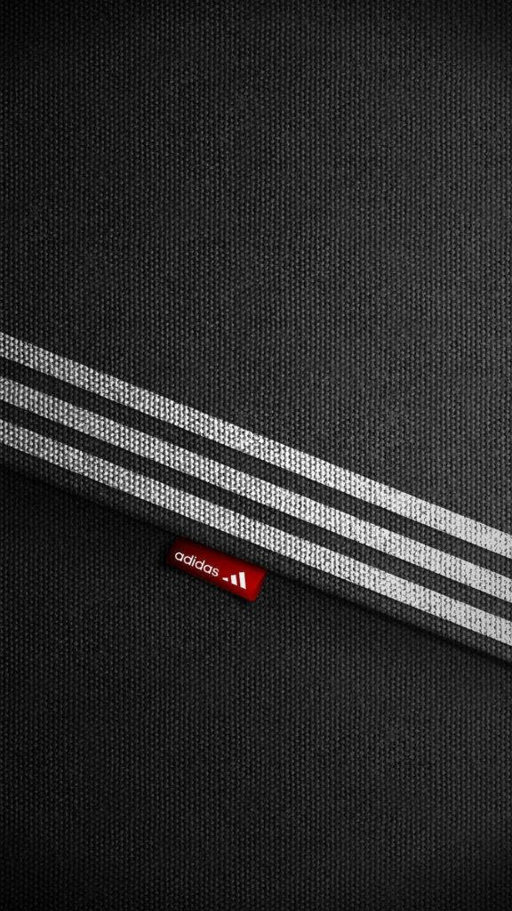 adidas iPhone 桌布 壁紙 — 黑色紋理布料特寫，帶有白色條紋和紅色 adidas 標誌標籤。