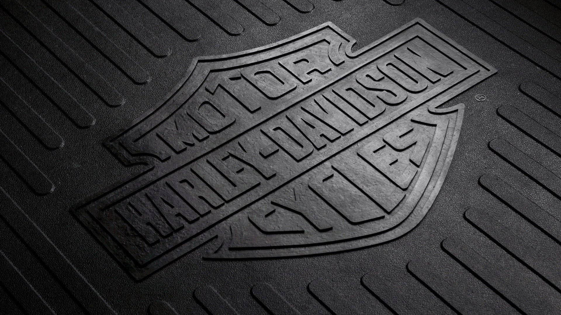Harley 桌布 壁紙 — 黑色紋理橡膠地墊的特寫，帶有浮雕哈雷戴維森標誌，微妙的燈光突顯其堅固表面。